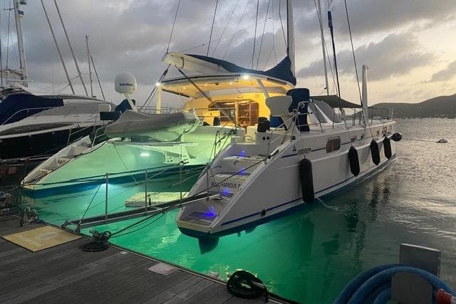2003 Catana 582 catamaran docked at sunset, illuminated with vibrant underwater lights.