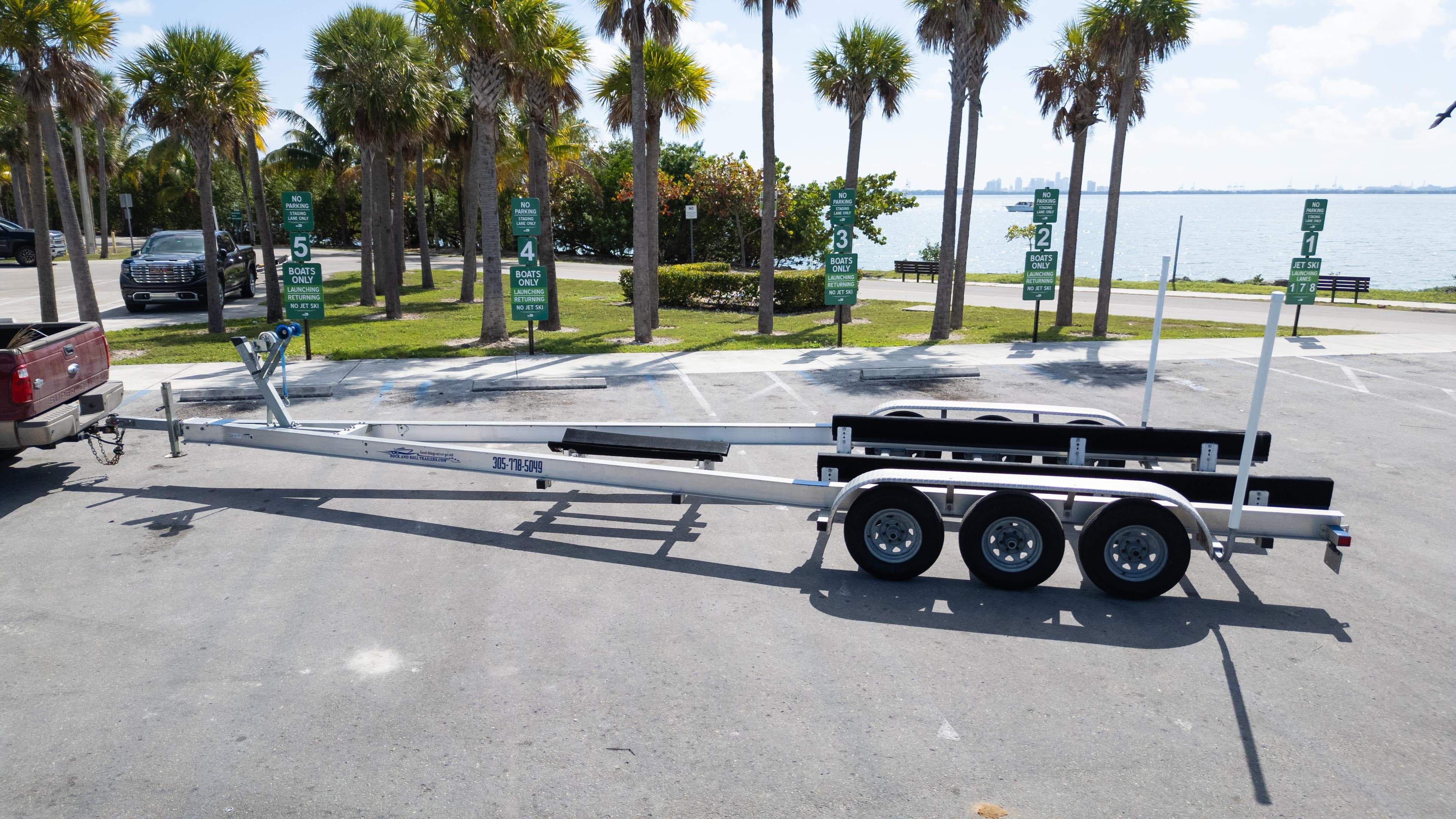 Trailer for 2019 Century 3200 Center Console boat, parked near palm trees by the water.