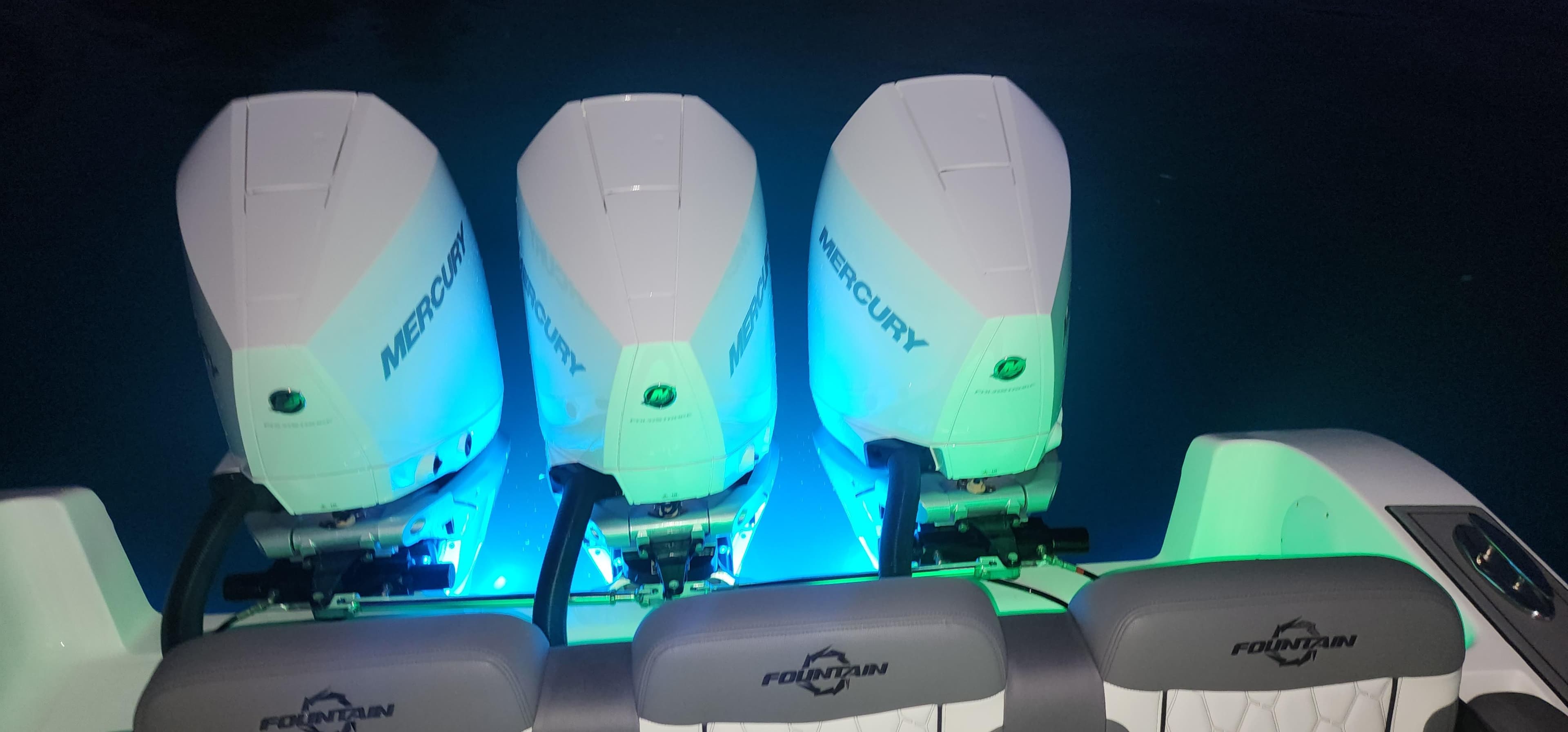 2023 Fountain 34 SC boat with triple Mercury engines illuminated at night.