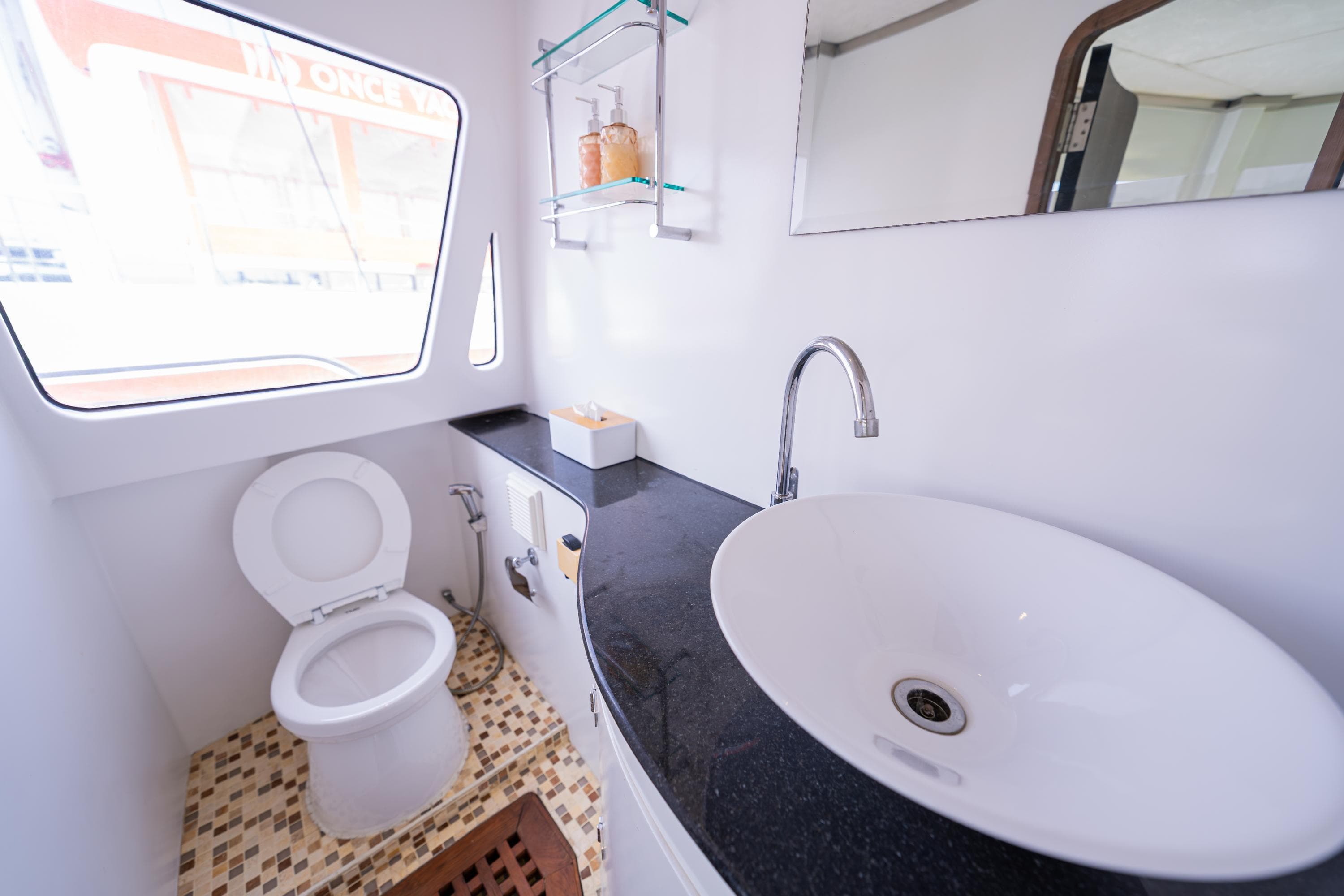 Modern bathroom in Custom Courage 82 yacht, featuring sleek sink, toilet, and window view.