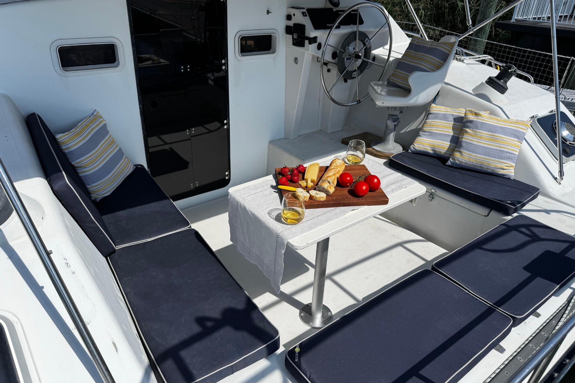 Cozy seating area on 1991 PDQ 36 yacht with snacks and drinks on table.