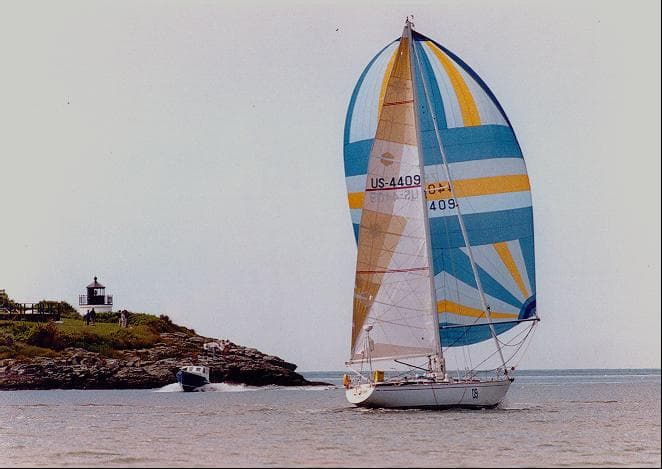 1973 Nautor Swan 44 sailboat with colorful spinnaker near a lighthouse.
