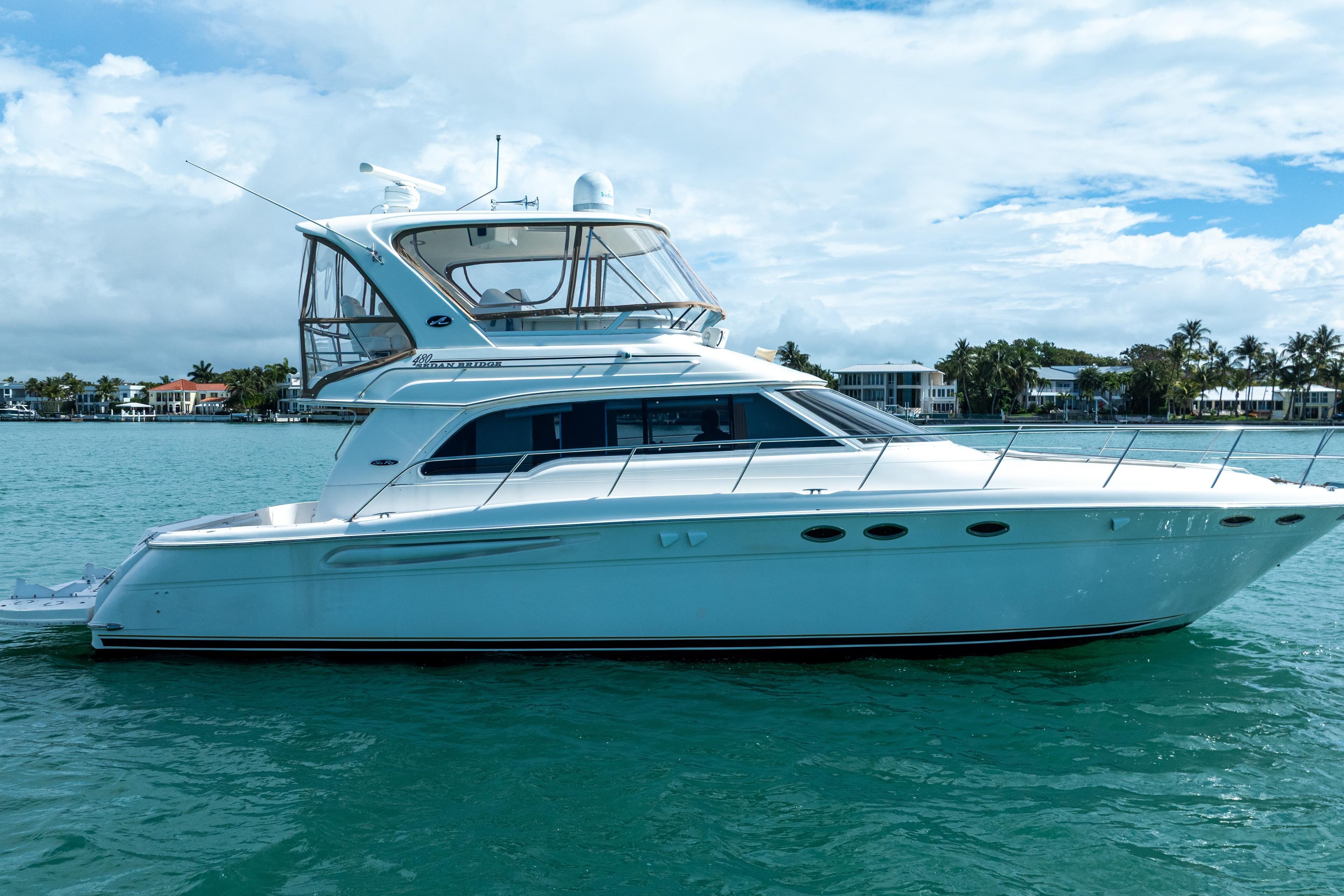 2003 Sea Ray 480 Sedan Bridge yacht on calm water, with coastal homes in the background.