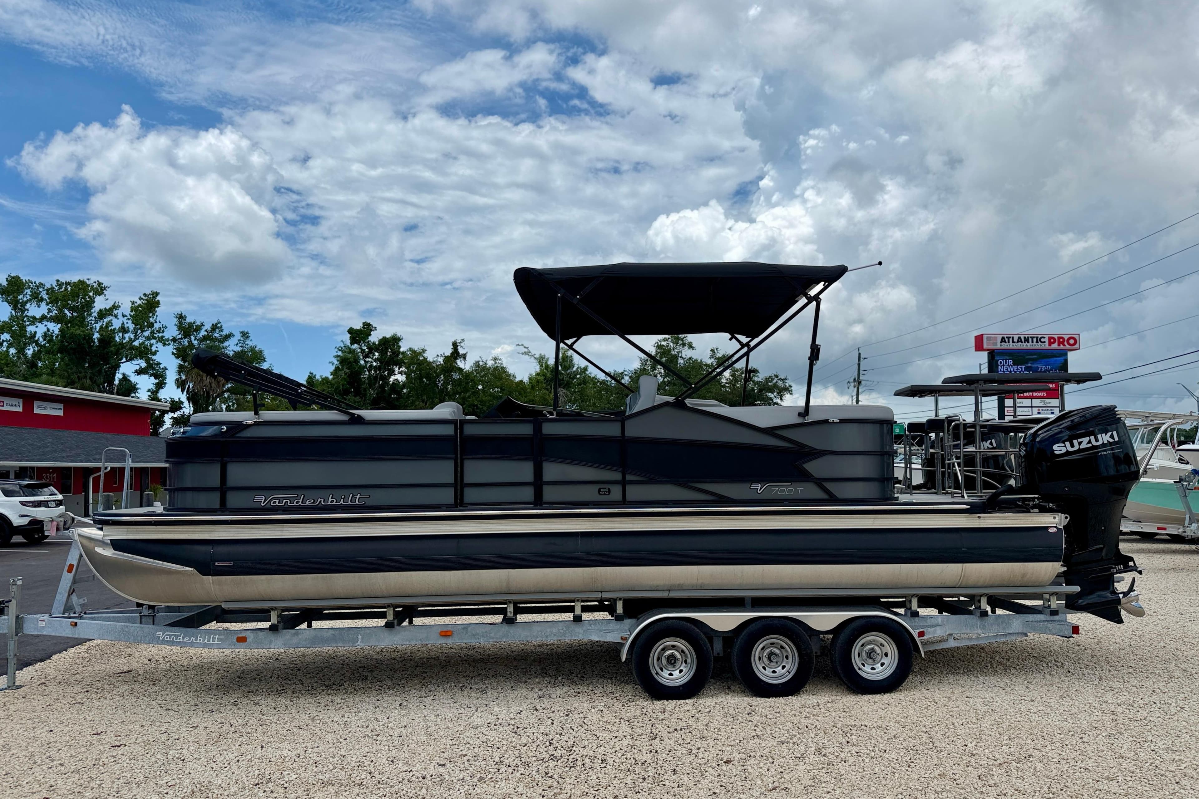 2025 Vanderbilt 700T pontoon boat on trailer, featuring Suzuki outboard motor, under cloudy sky.