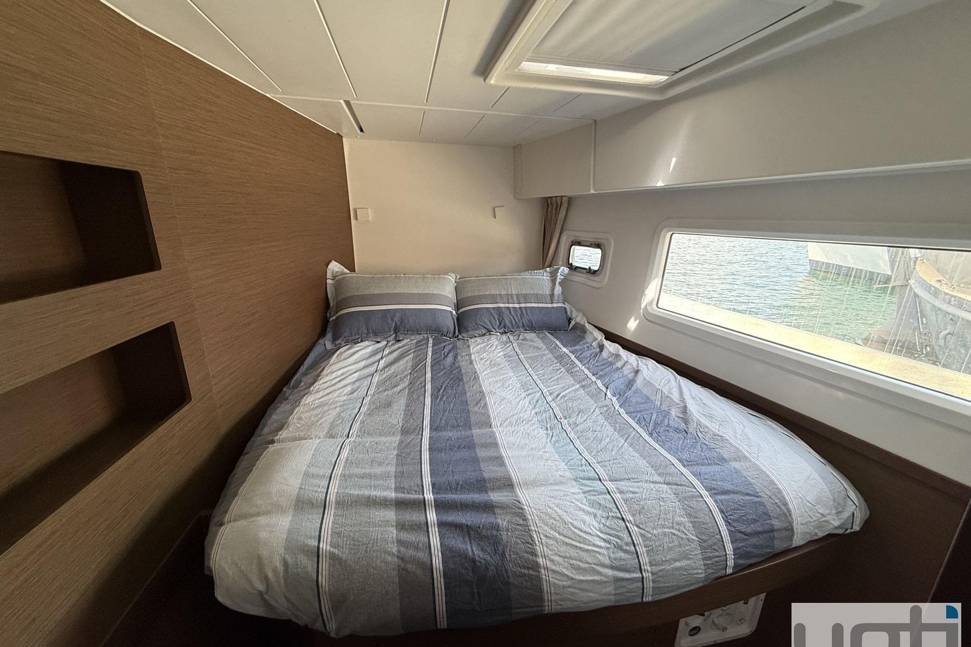 Cozy cabin interior of 2019 Lagoon 42 catamaran with striped bedding and ocean view.