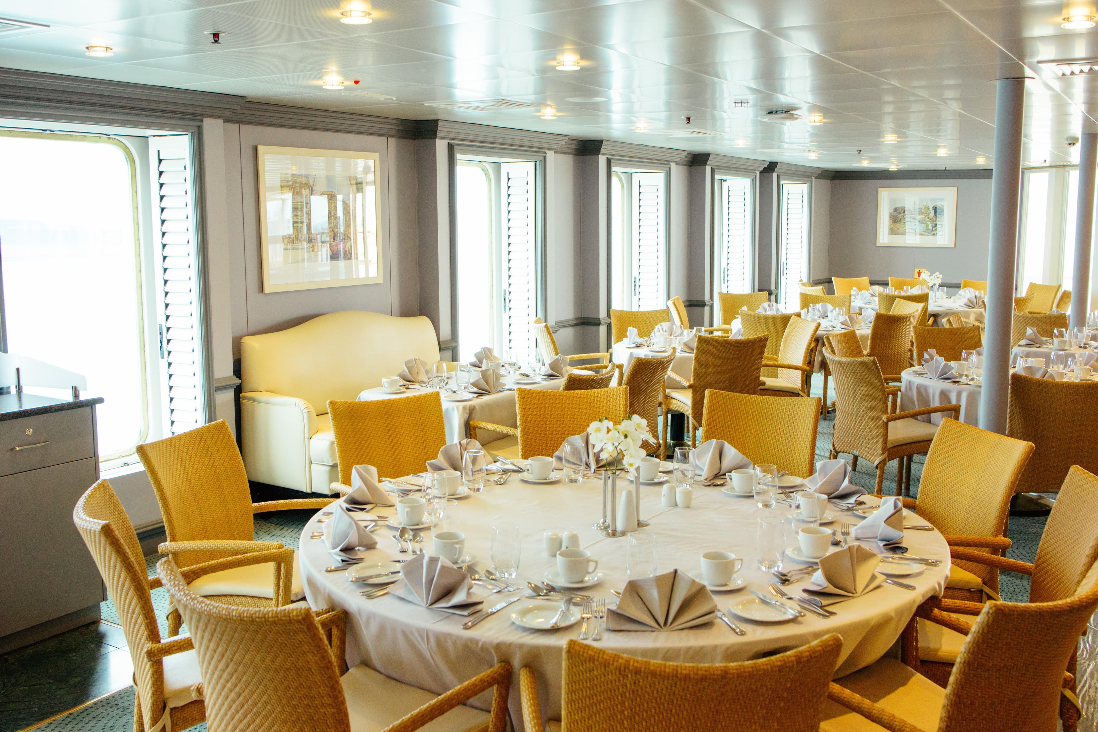 Elegant dining room on 1996 Minerva cruise ship with neatly set tables and wicker chairs.