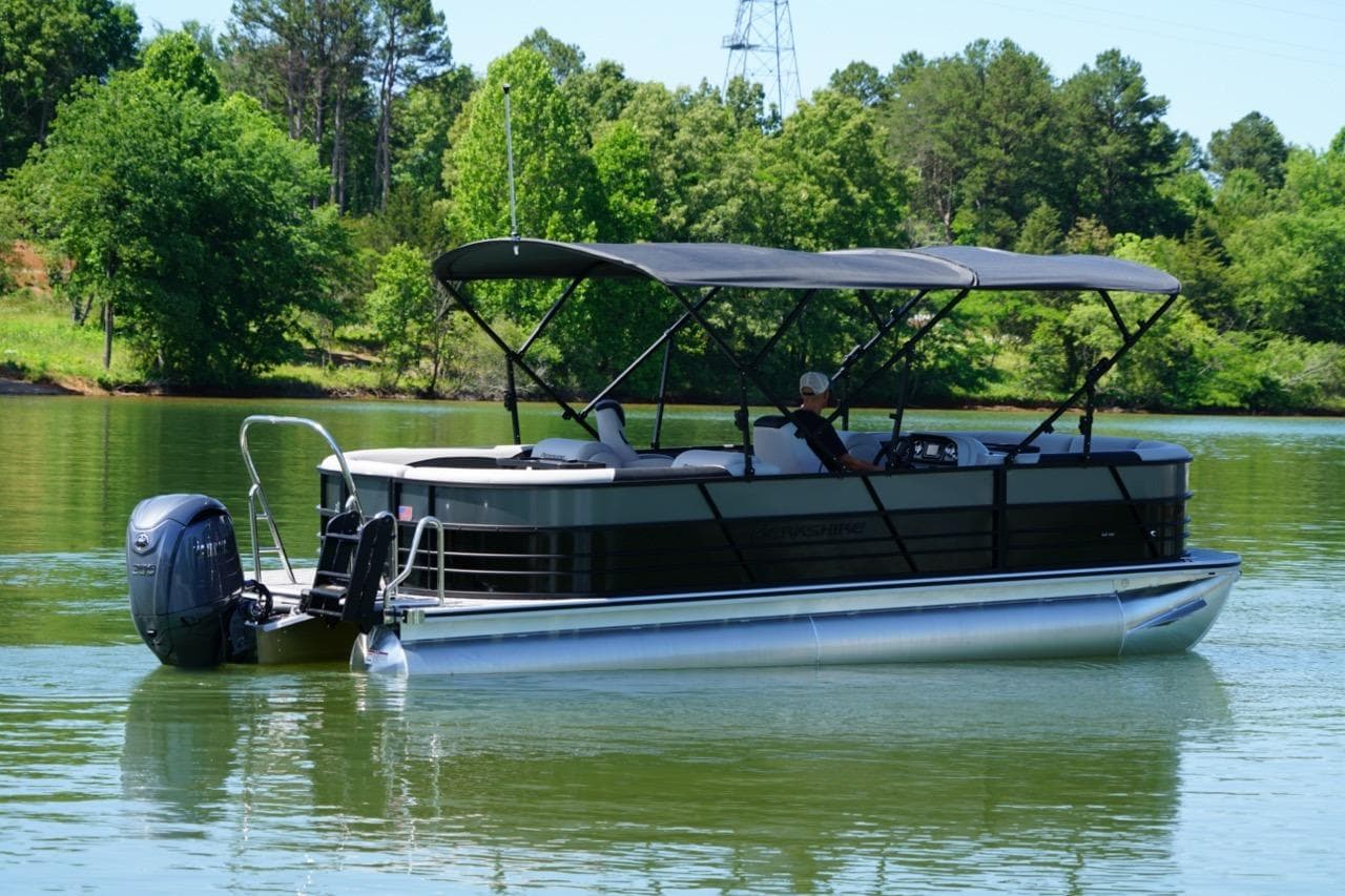 2026 Berkshire 24 RFX LE pontoon boat cruising on a serene lake with lush greenery.
