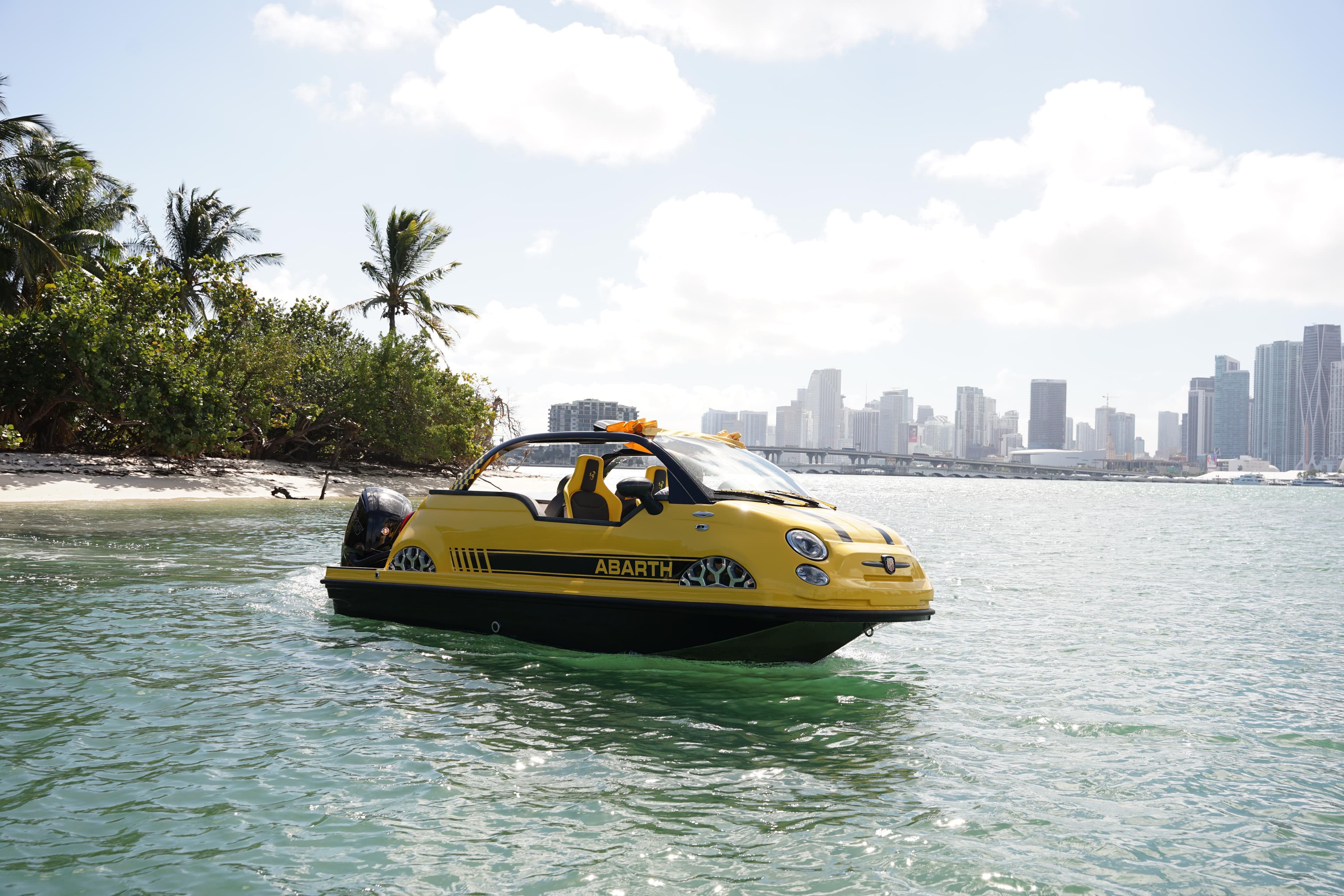 2025 Car Off-shore Fiat 500 Abarth boat on water near tropical shoreline and city skyline.