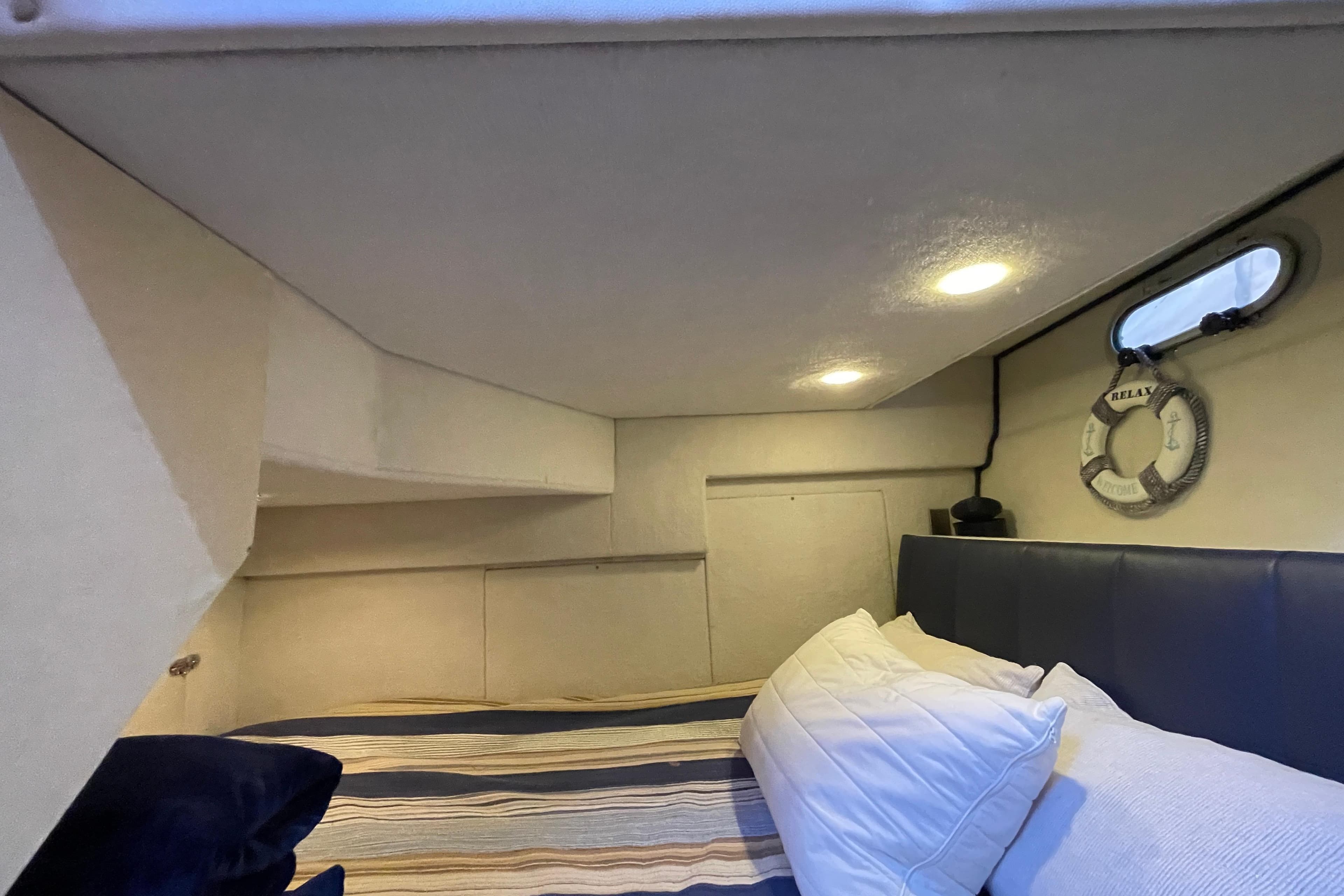 Cozy cabin interior of 1995 Bayliner 3988 Motoryacht with striped bedding and porthole.