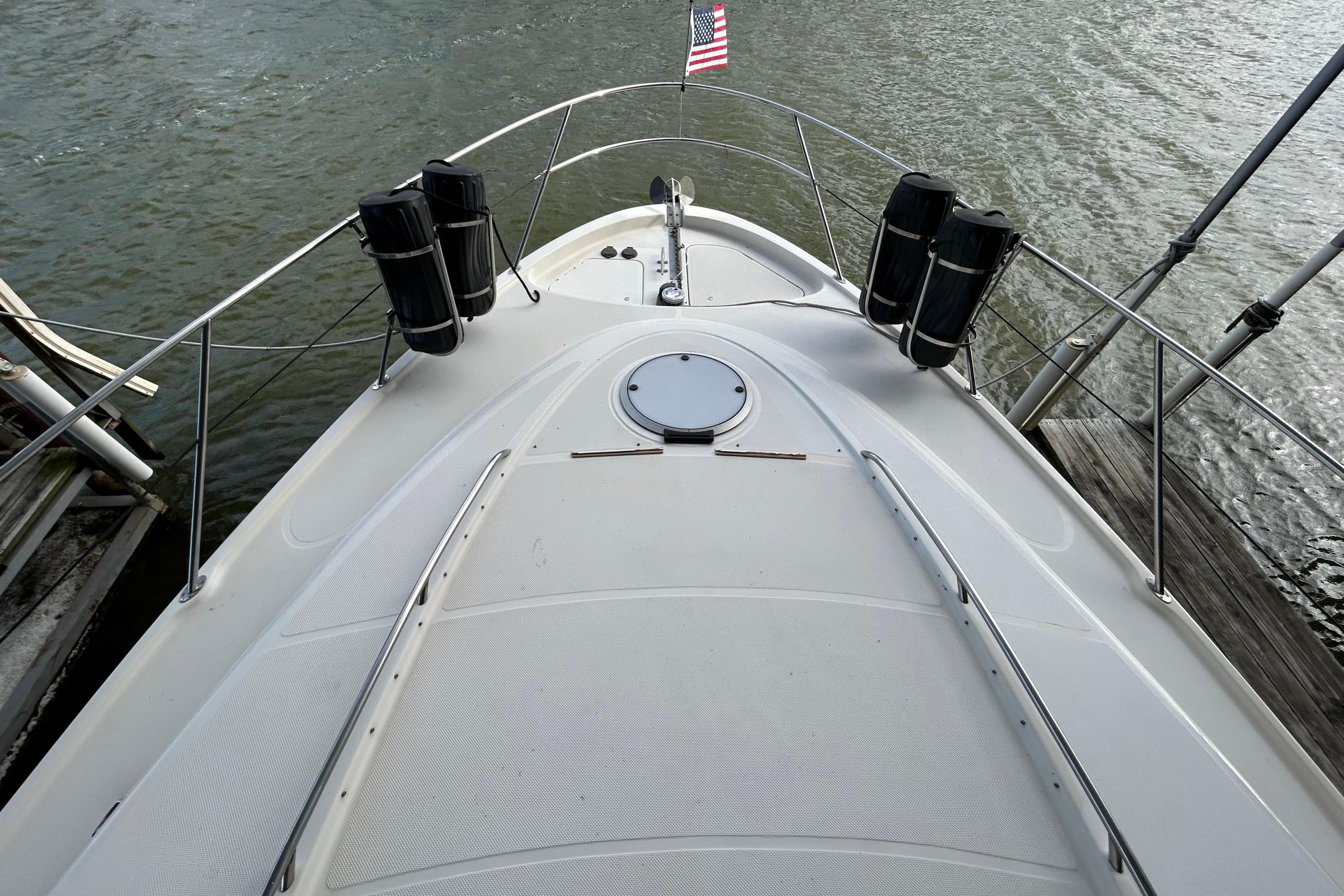 1999 Maxum 4600 SCB yacht bow view with American flag, docked on water.
