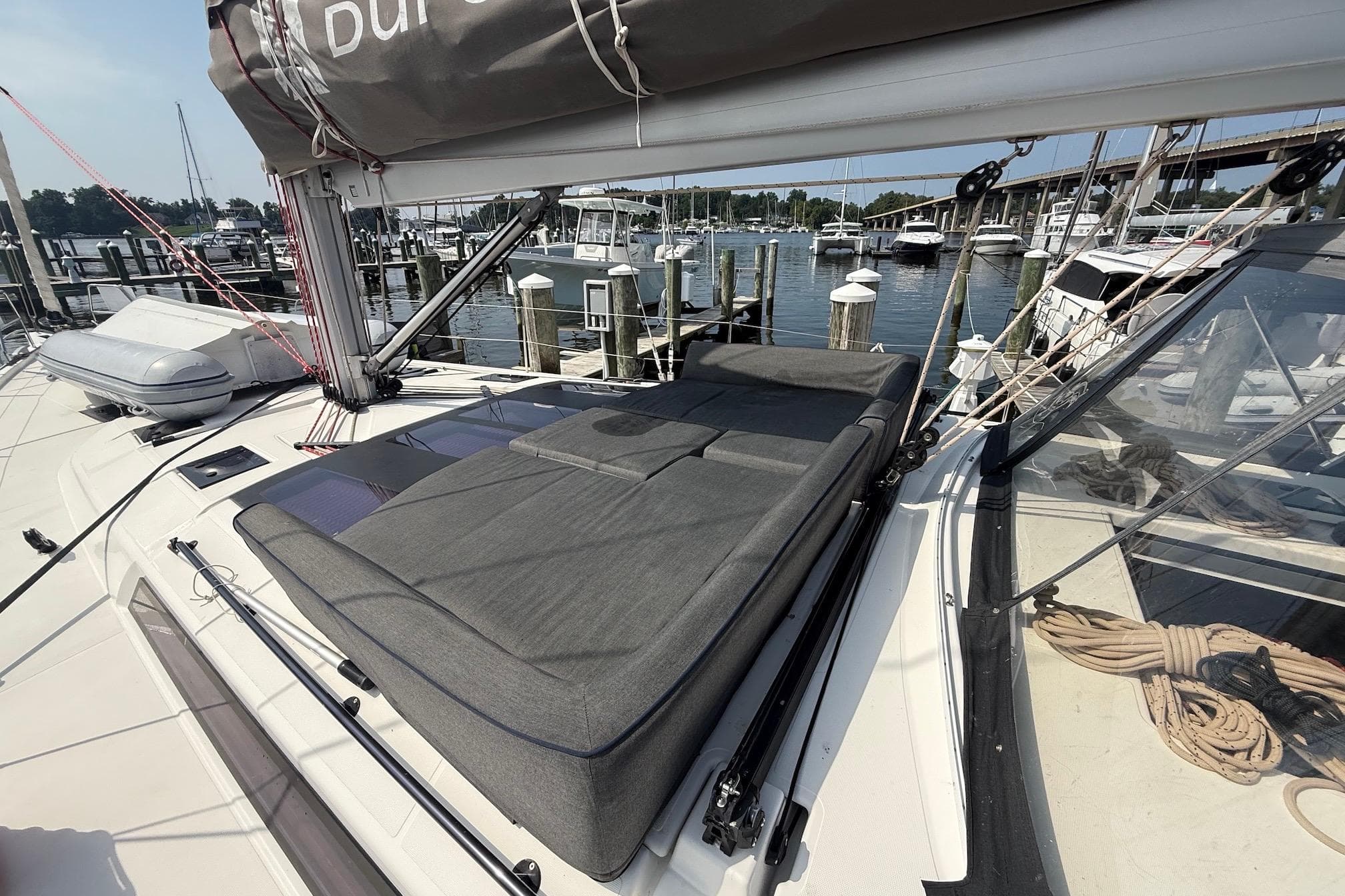 2022 Dufour 530 yacht with cushioned deck, docked at marina with boats and bridge.