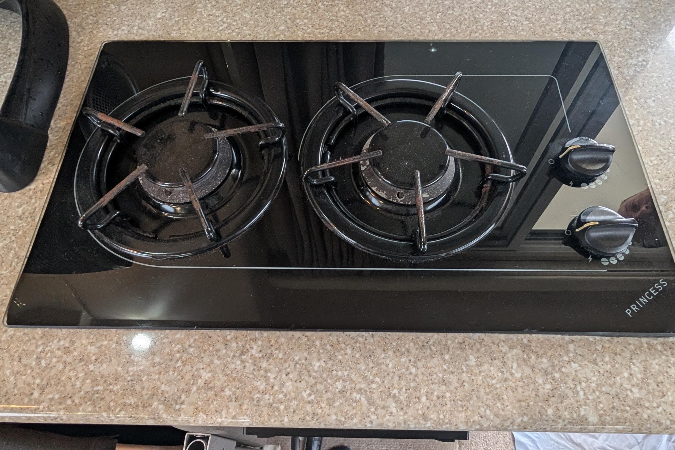 Two-burner black gas stove on a granite countertop, featuring control knobs.