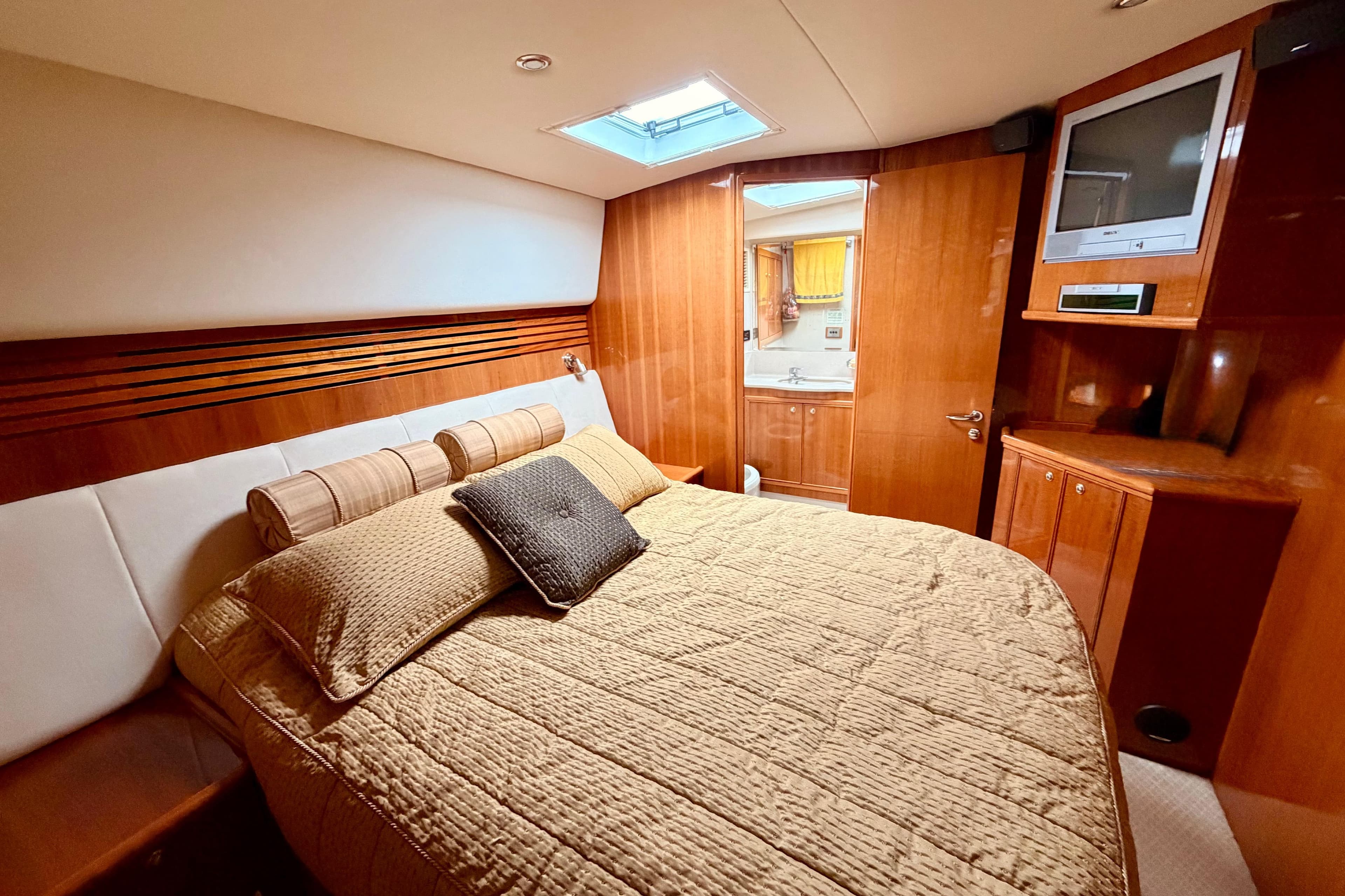Luxurious bedroom interior of 2004 Riviera 60 Flybridge yacht with wood paneling and cozy bedding.