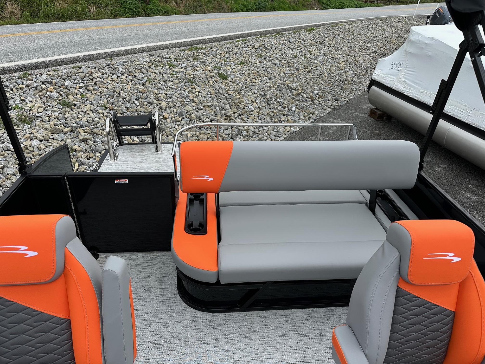 2025 Bennington 22 SSB Swing Back boat with orange and gray seating, docked near a road.