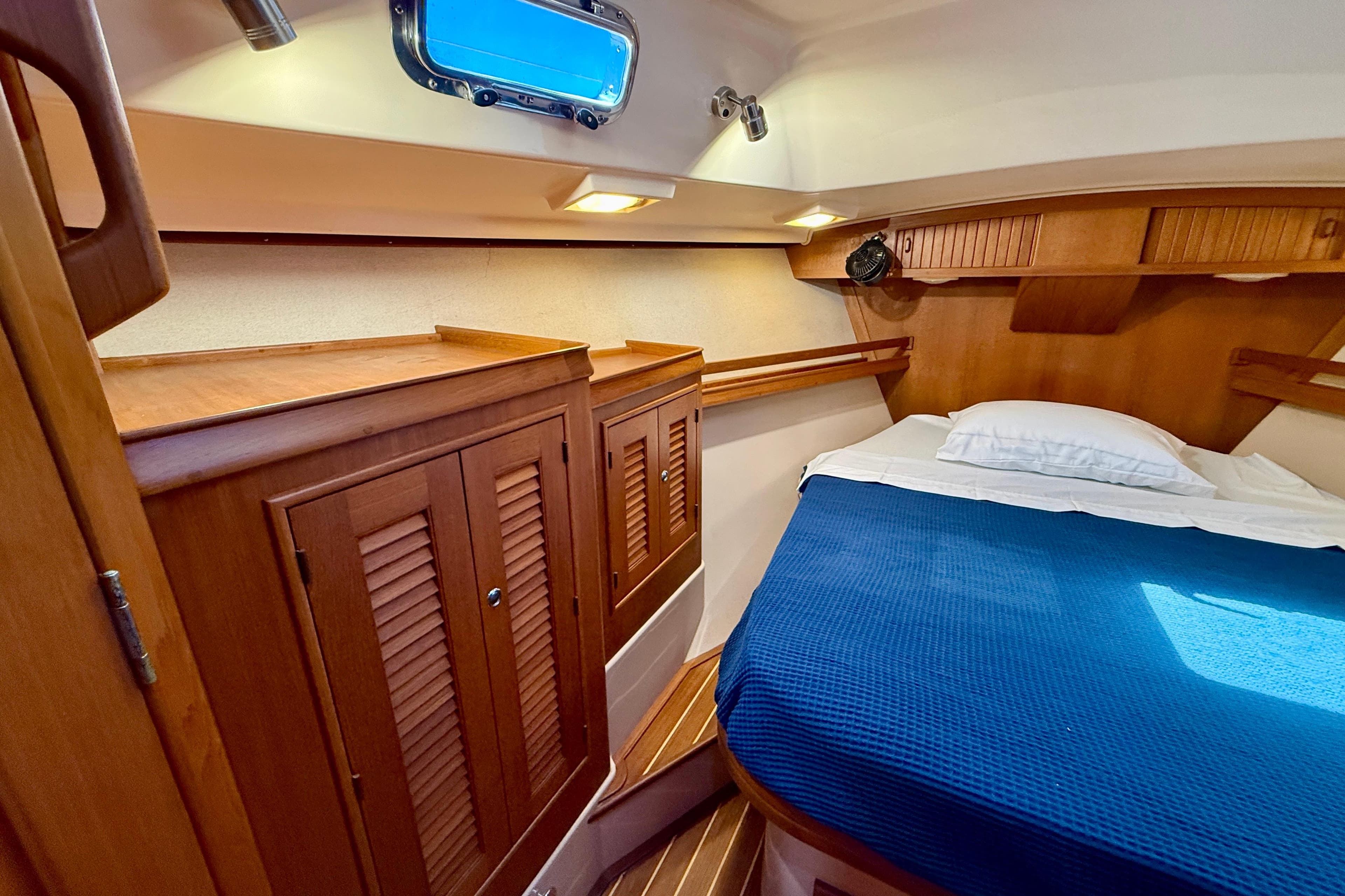 Cozy cabin interior of 2006 Island Packet 485 yacht with wooden cabinetry and blue bedding.