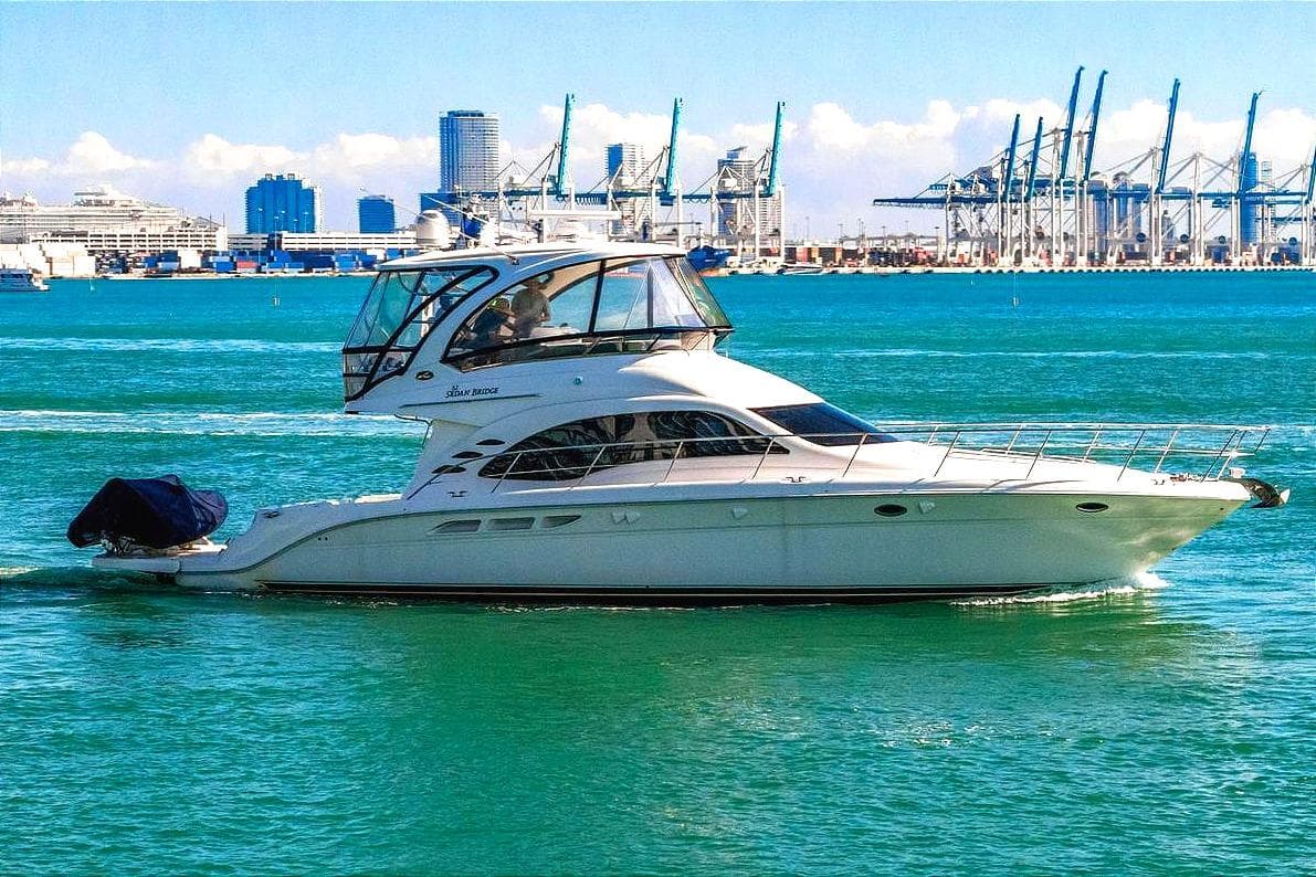 2007 Sea Ray 52 Sedan Bridge yacht cruising in a vibrant harbor with cityscape backdrop.