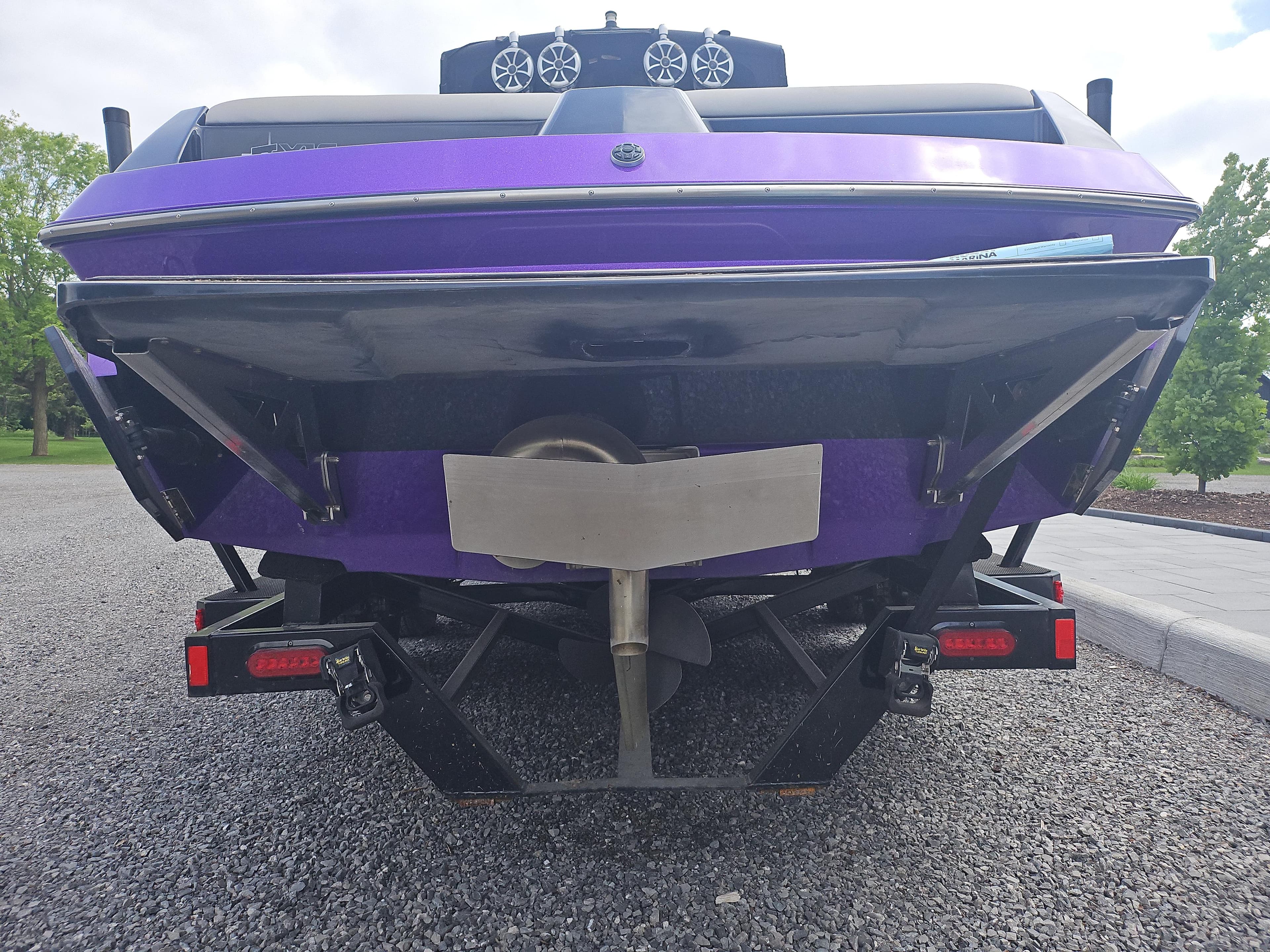2015 Axis A24 boat, rear view, purple hull, parked on gravel.