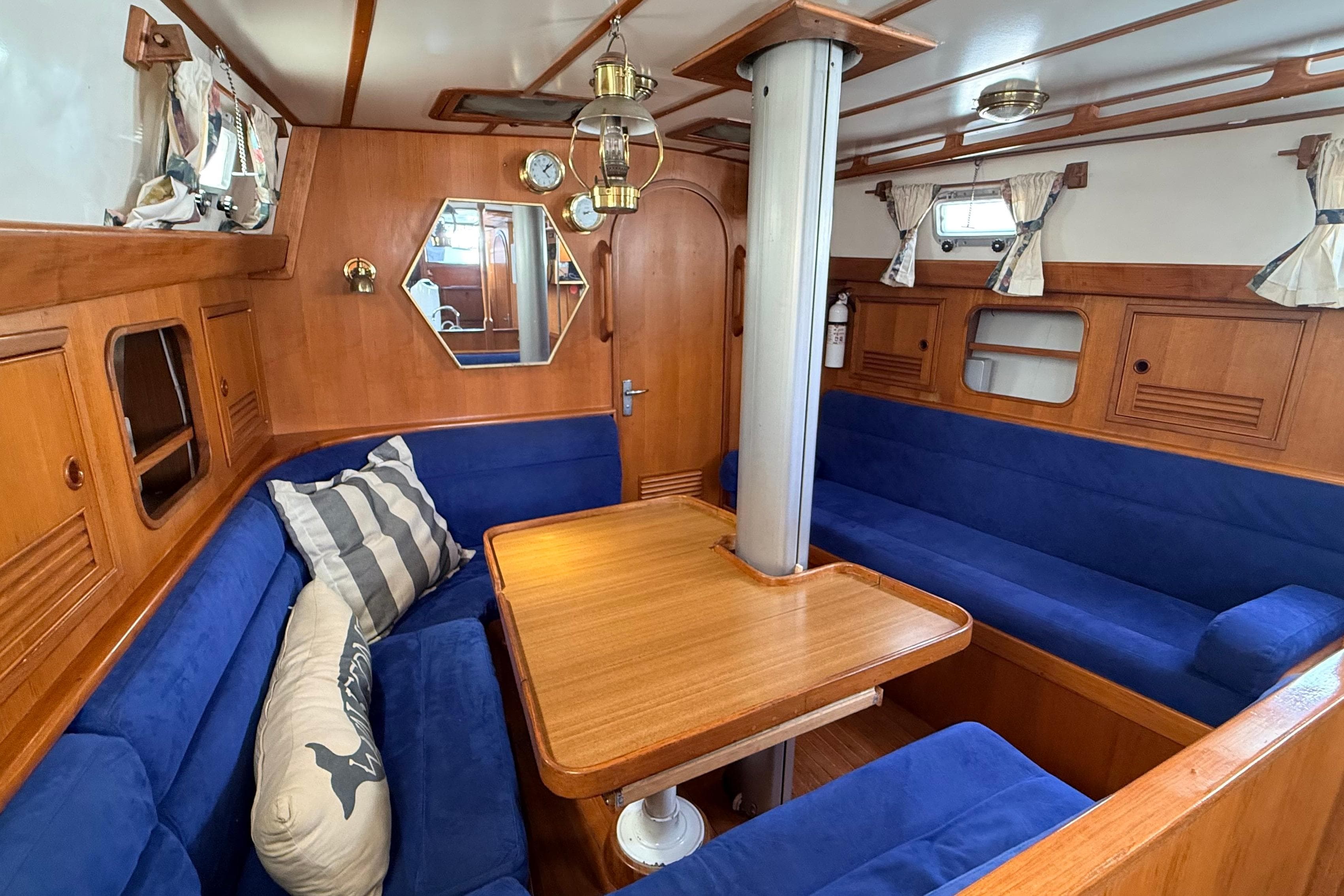 Cozy 1983 Tanton 44 yacht interior with blue seating, wooden table, and nautical decor.