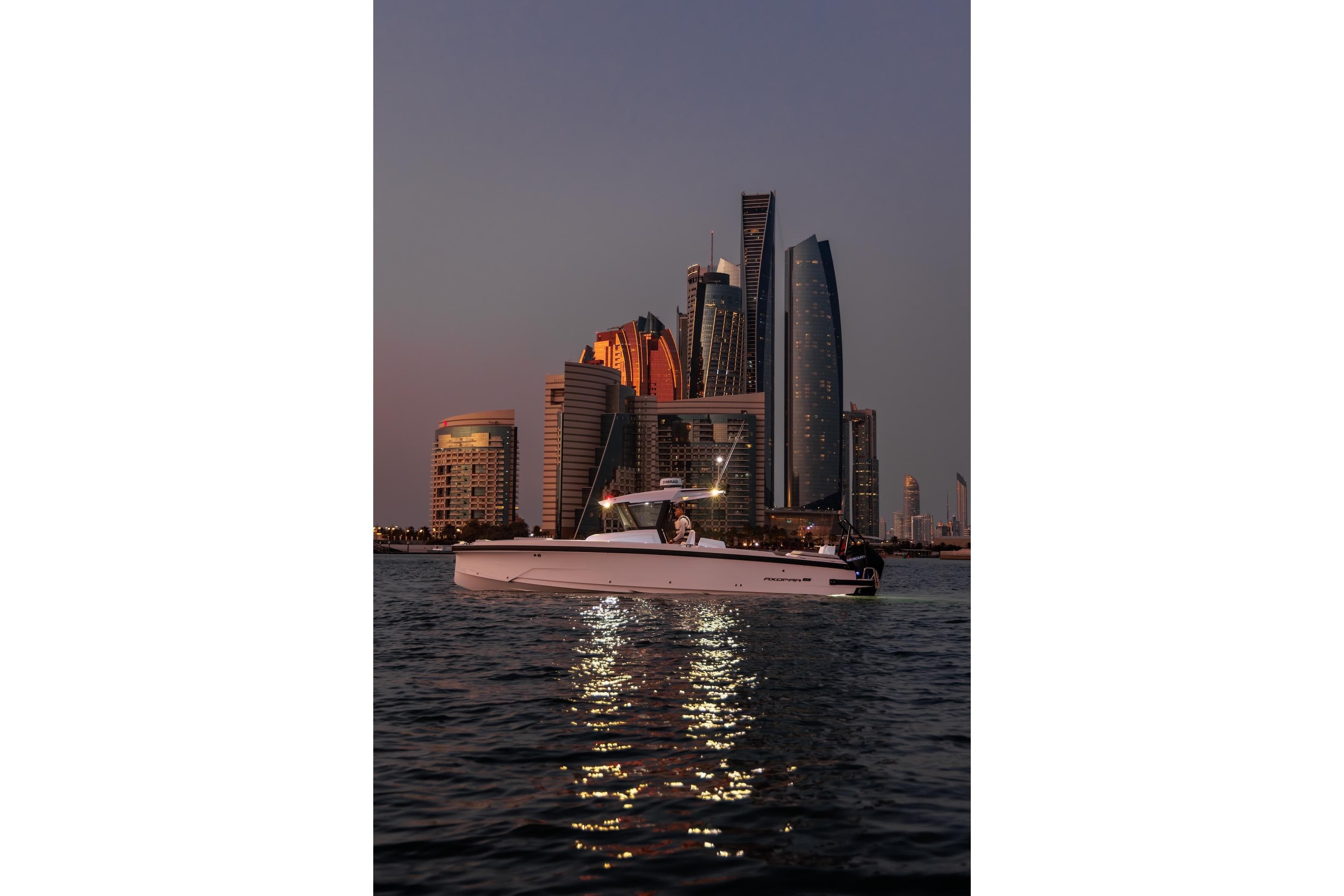 2026 Axopar 29 CCX boat cruising at sunset with city skyline backdrop.
