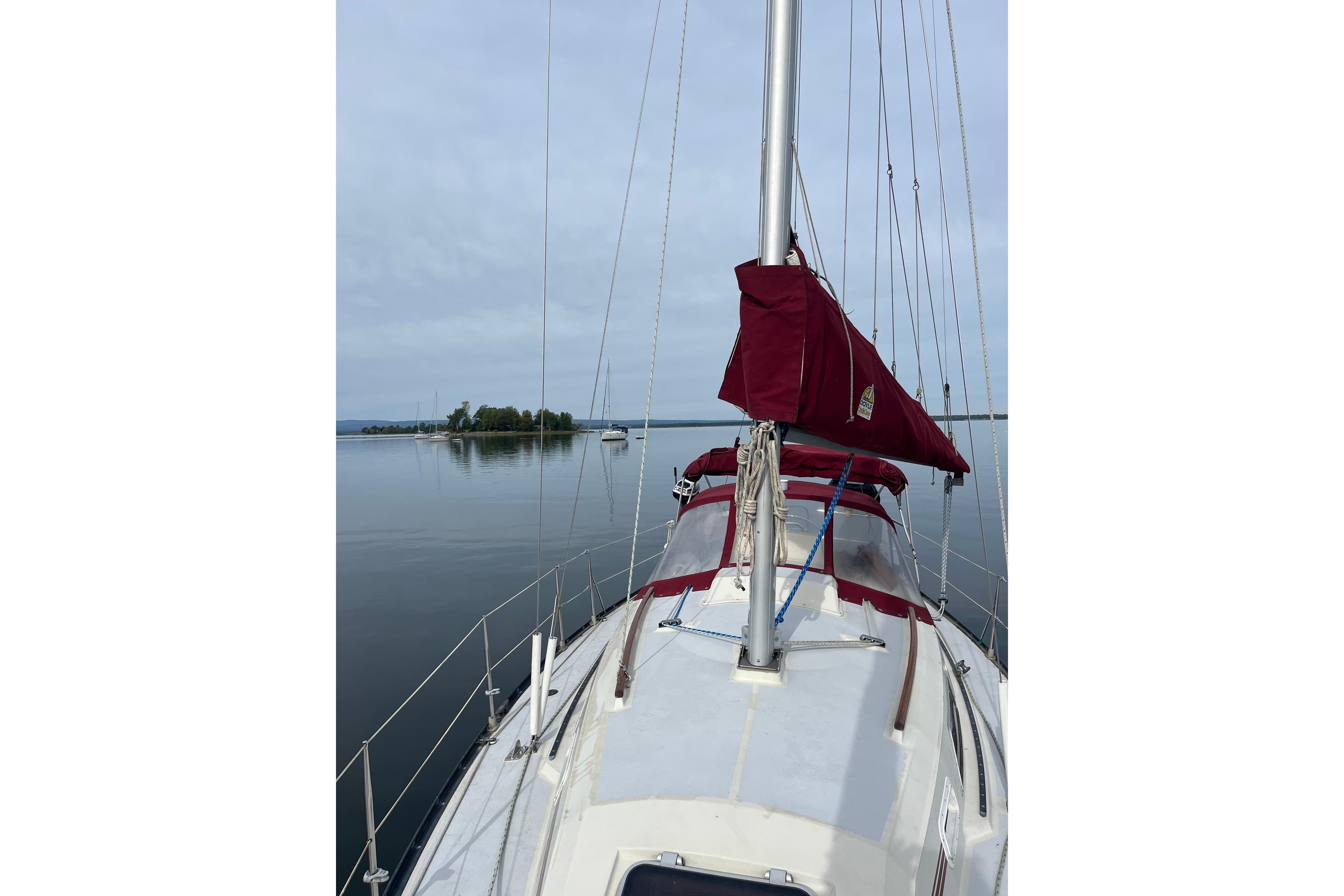 1988 Mirage 32 sailboat with red sail cover on calm water, distant island view.
