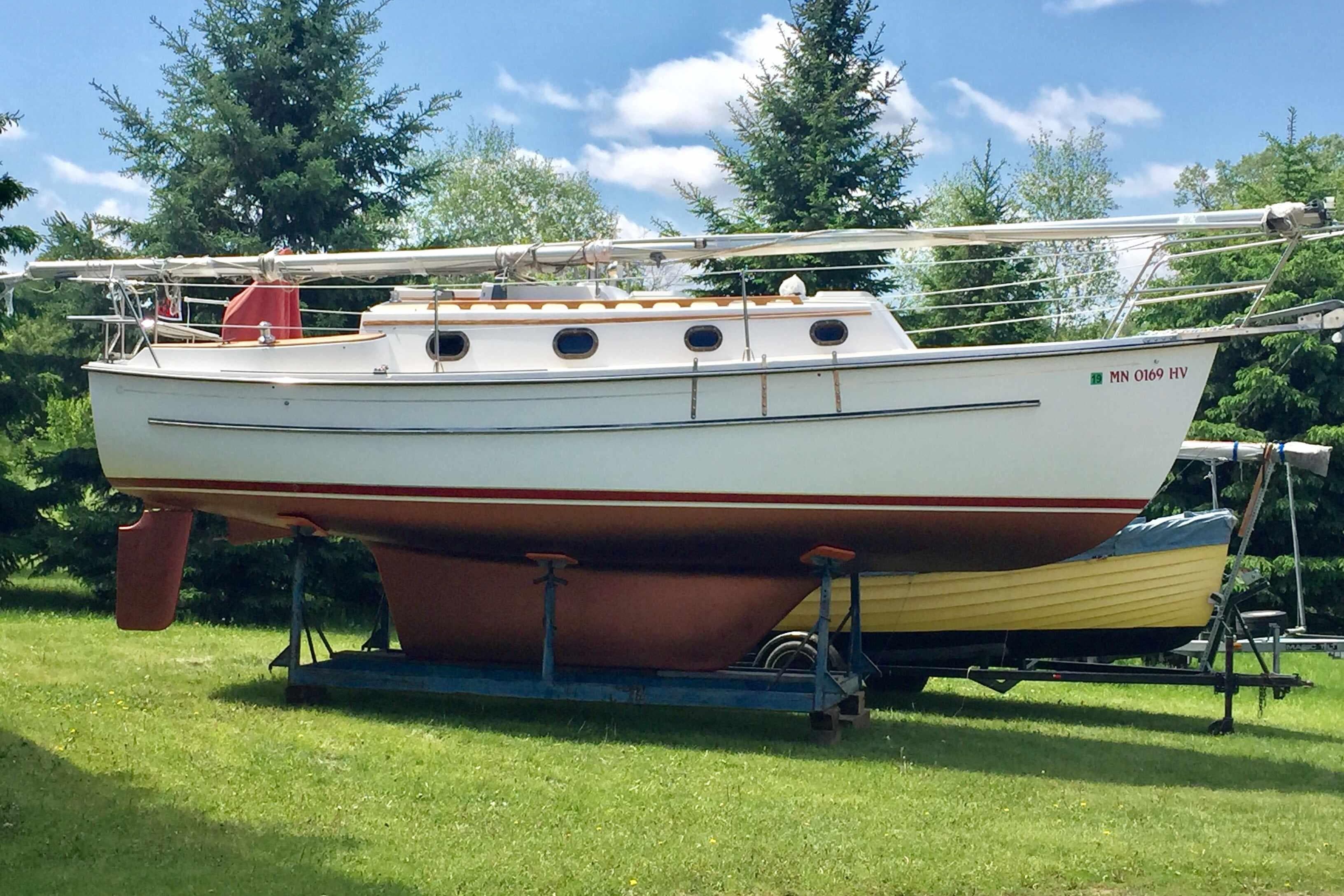 1997 Com Pac 27-2 sailboat on trailer, surrounded by trees under a blue sky.