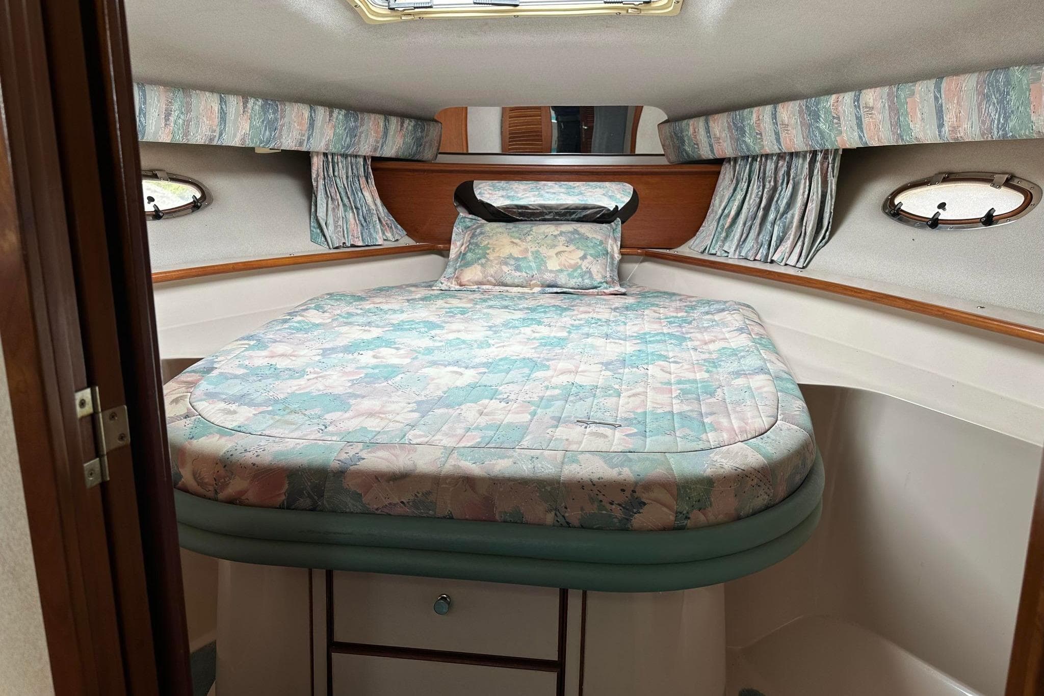 Cozy cabin interior of 1992 Regal Commodore 400 with floral bedding and porthole windows.