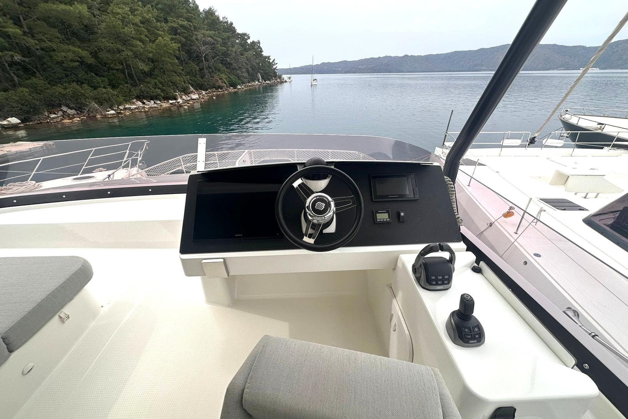 Helm of 2021 Fountaine Pajot Motor Yacht 44 overlooking serene waters and lush shoreline.