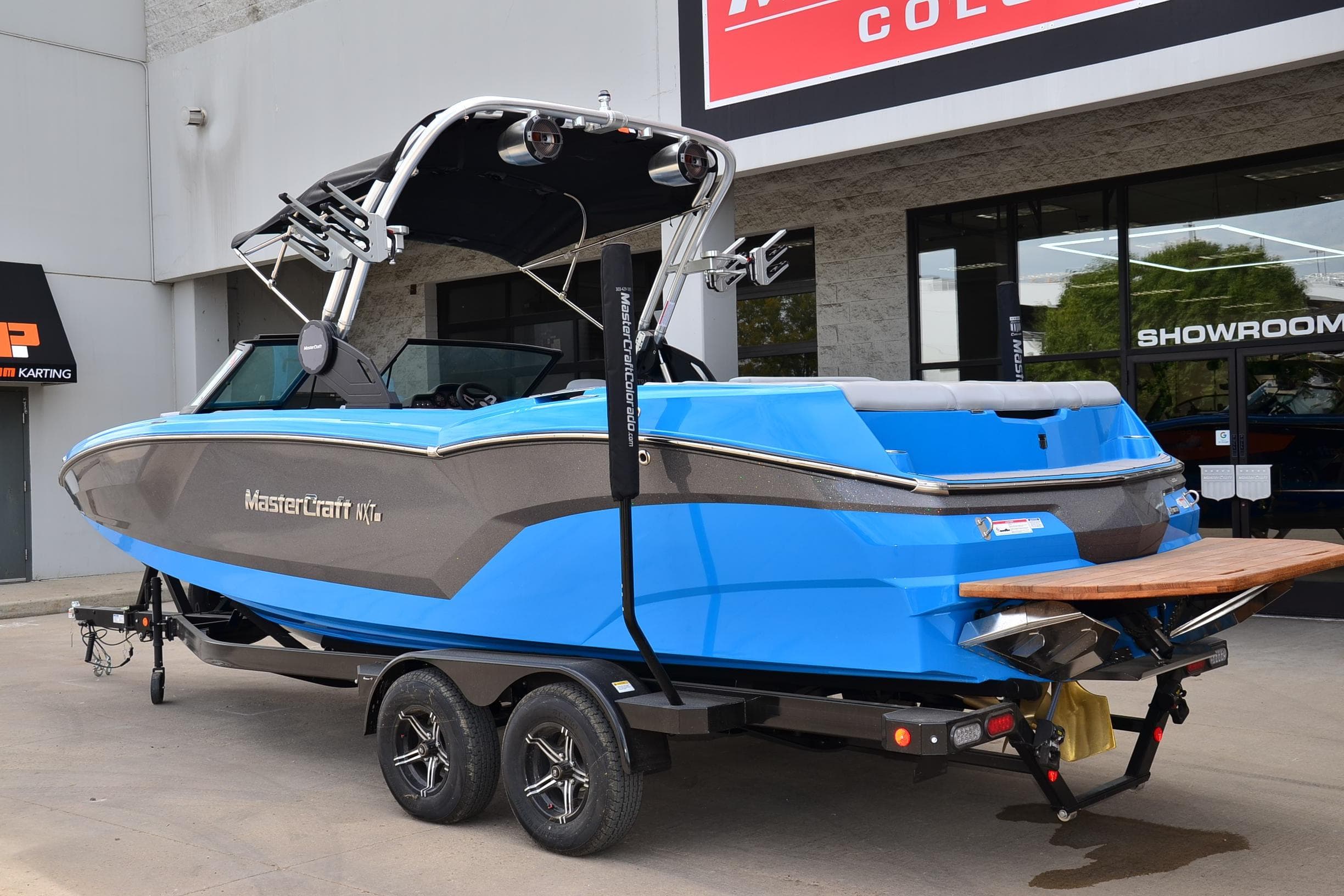 2022 MasterCraft NXT24 boat in blue, parked outside a showroom on a trailer.