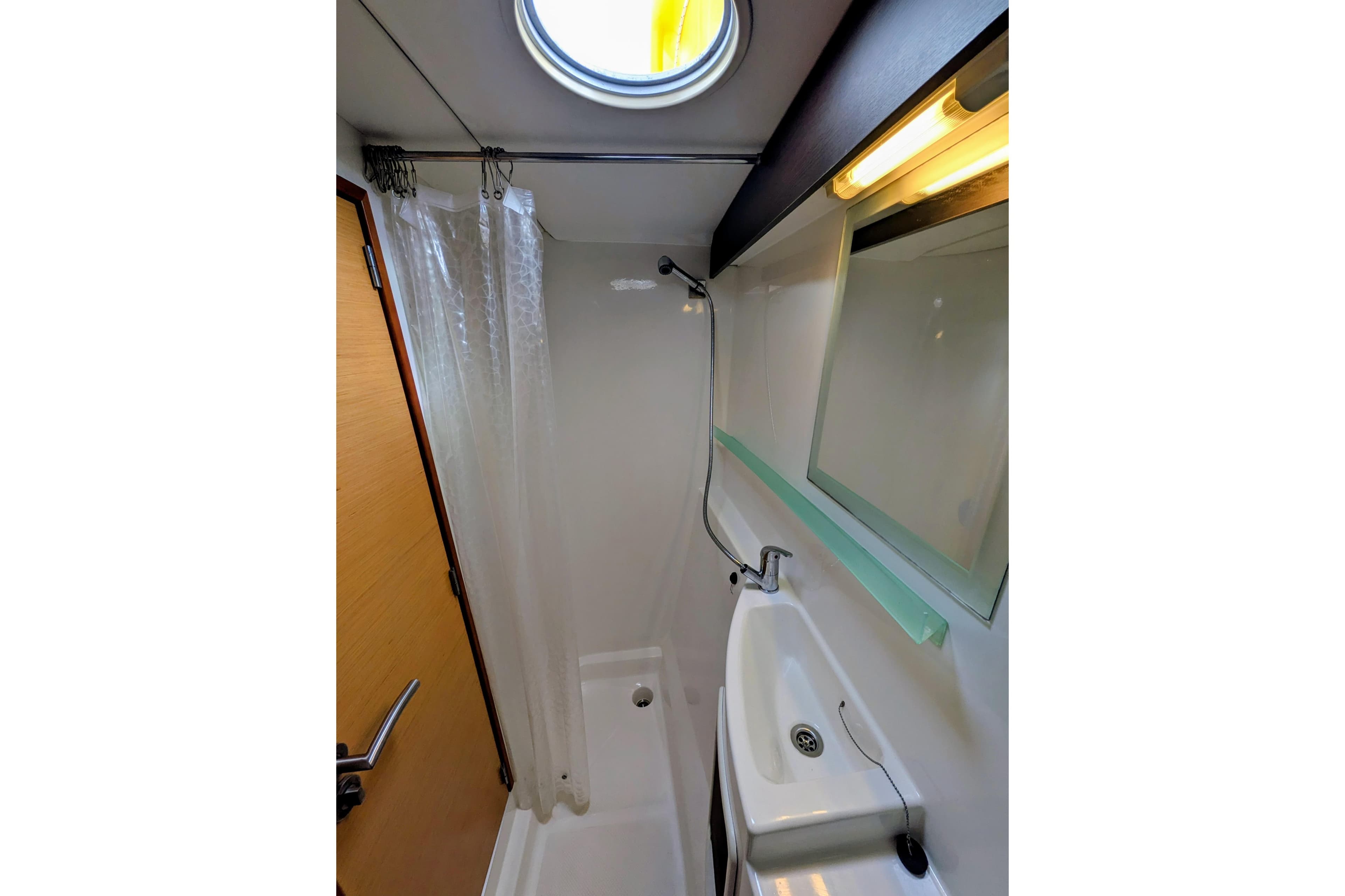 Compact bathroom in 2012 Fountaine Pajot Lipari catamaran with shower, sink, and porthole.