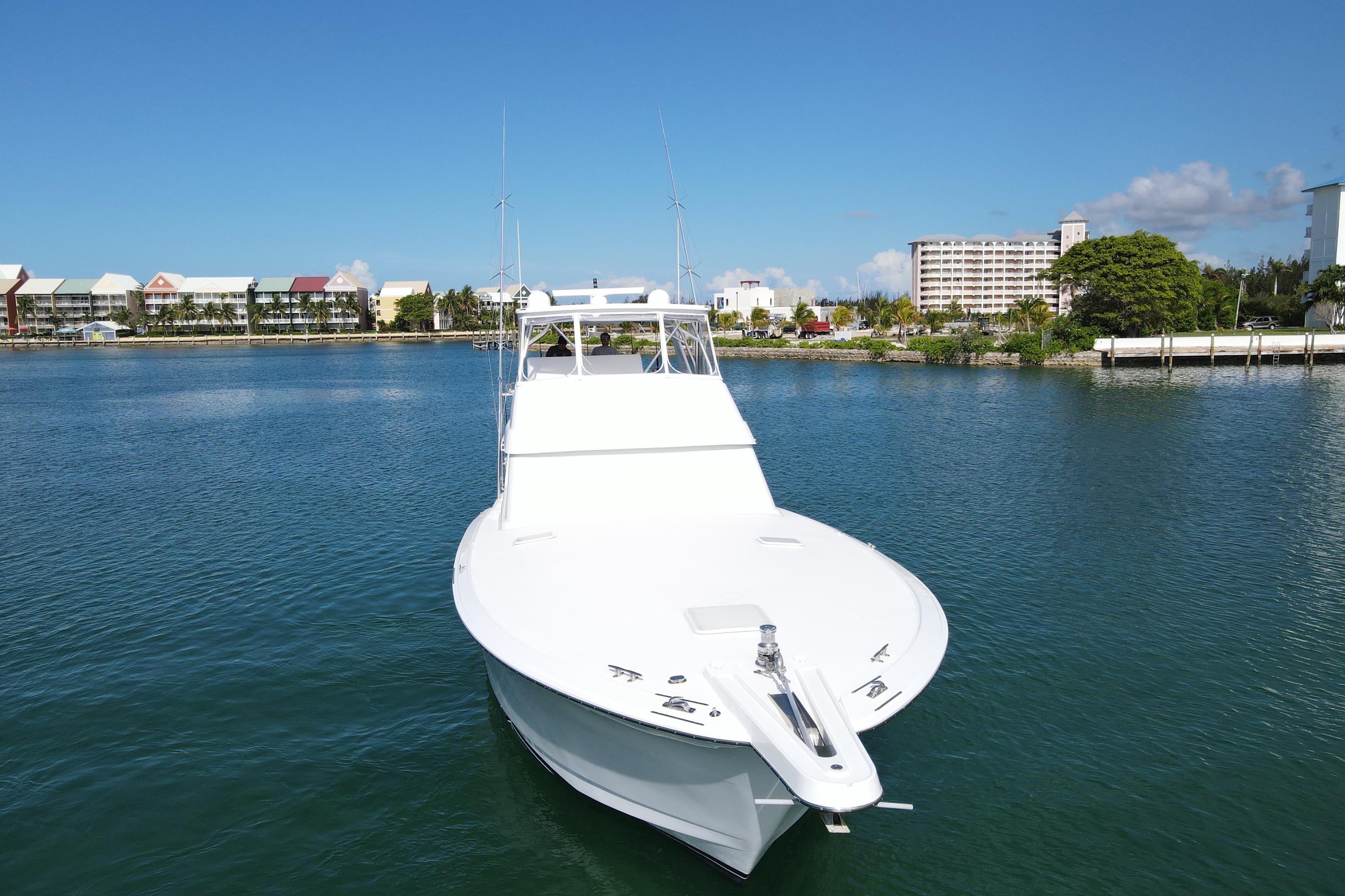 2004 Hatteras 60 Convertible yacht on calm water with coastal buildings in the background.
