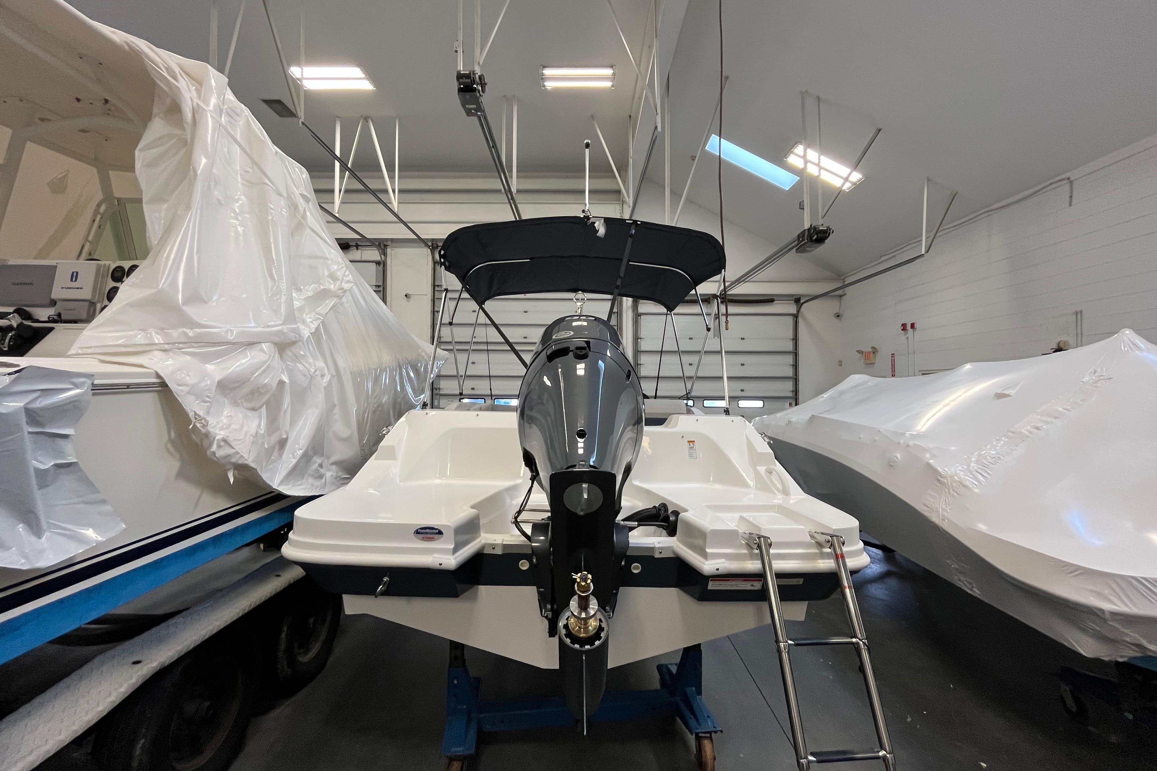 2026 Hurricane SunDeck Sport 185 OB boat in storage, rear view with motor and ladder.