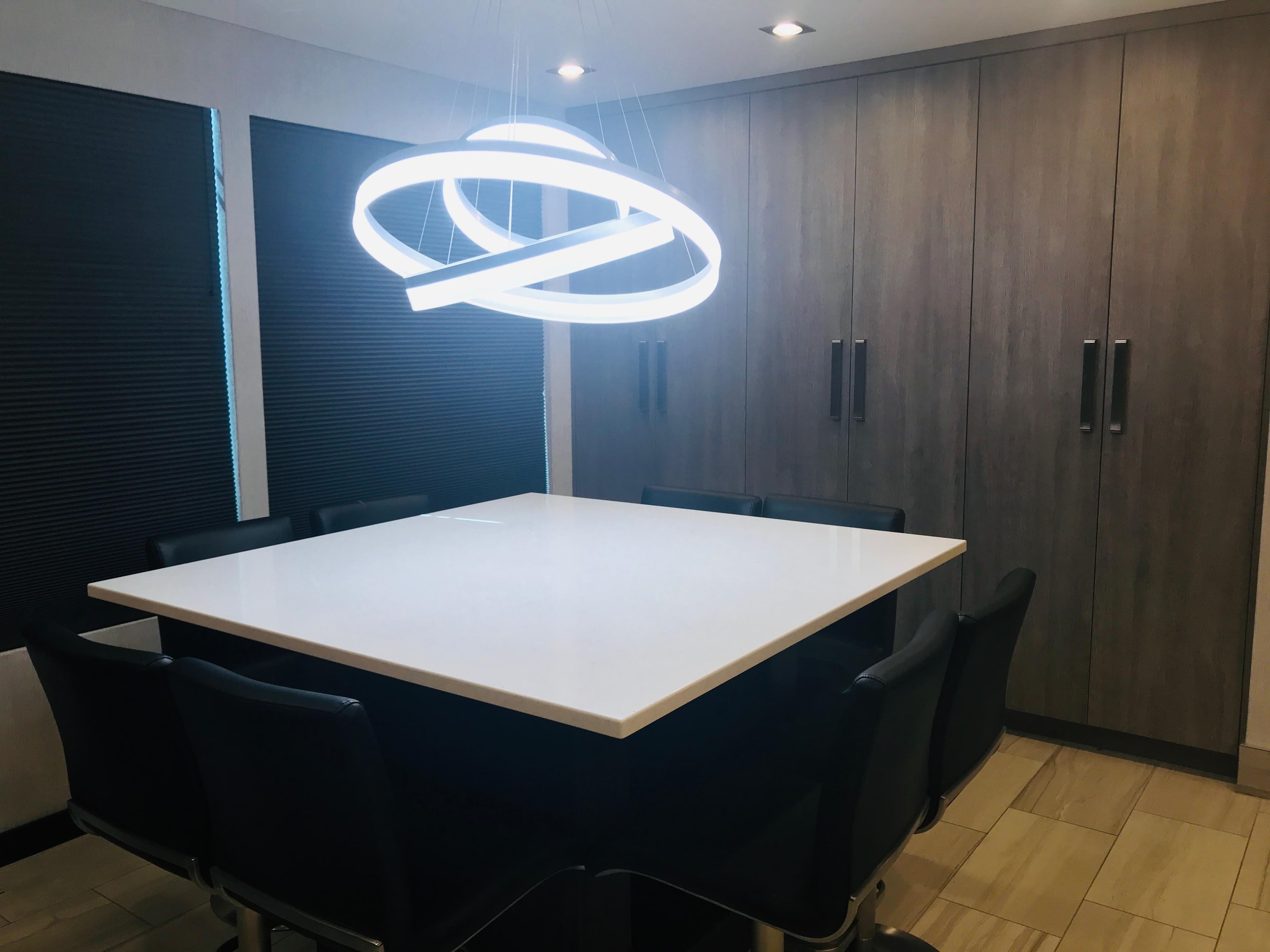 Modern dining room with square table, stylish chairs, and unique circular light fixture.