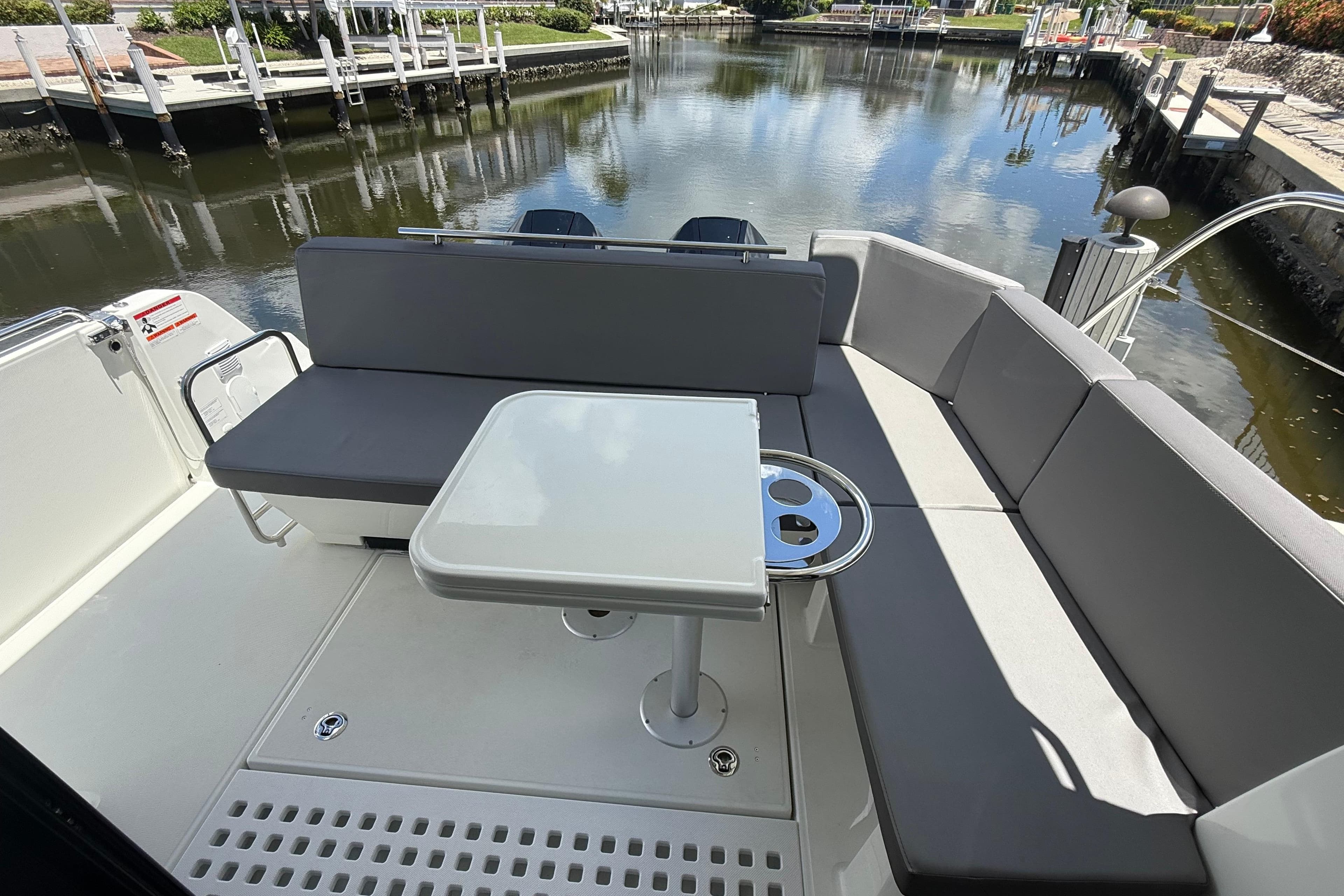2024 Beneteau Antares 11 boat interior with seating and table, docked by a calm waterway.