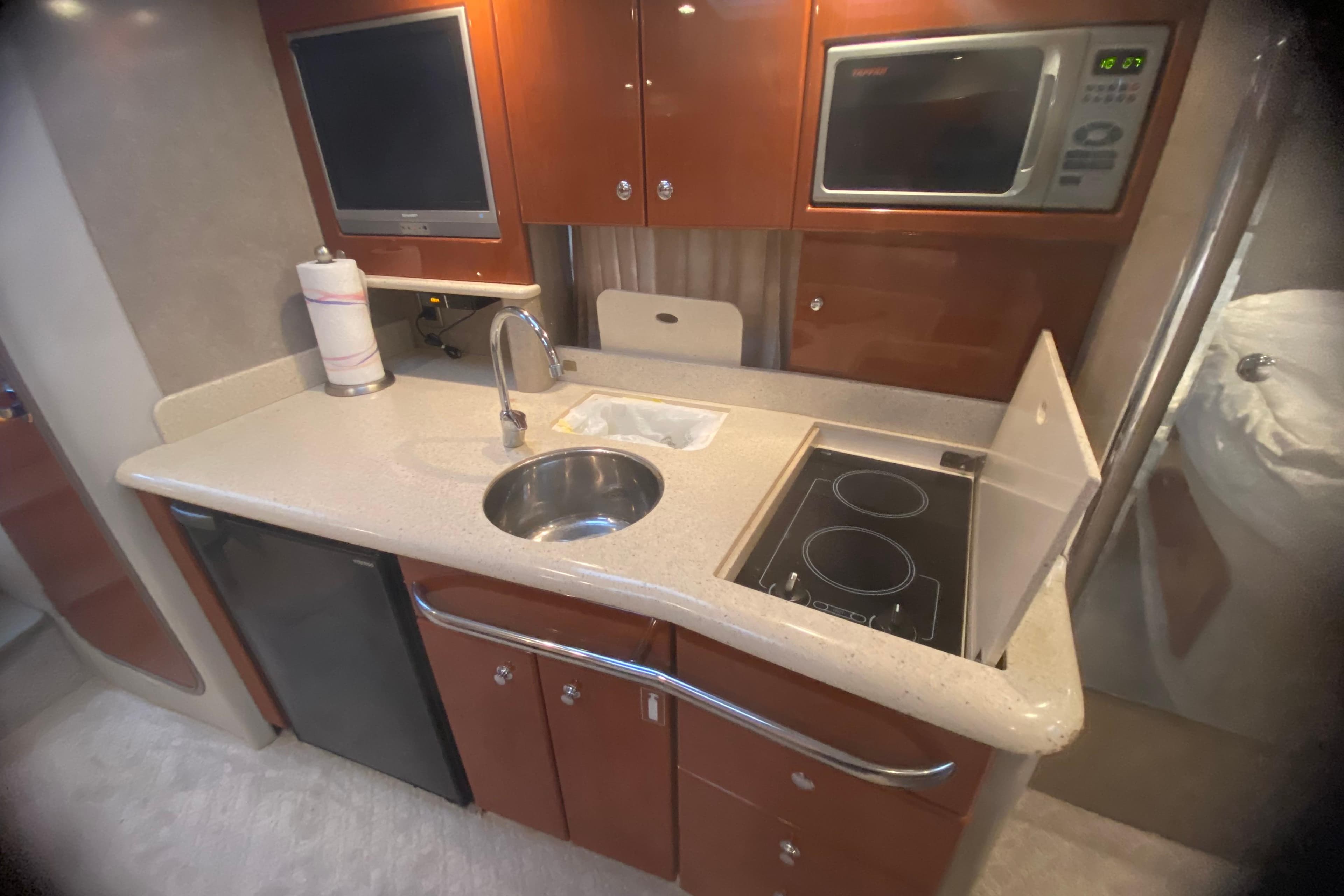 Compact yacht kitchen with sink, stove, microwave, and TV, featuring wood cabinetry.