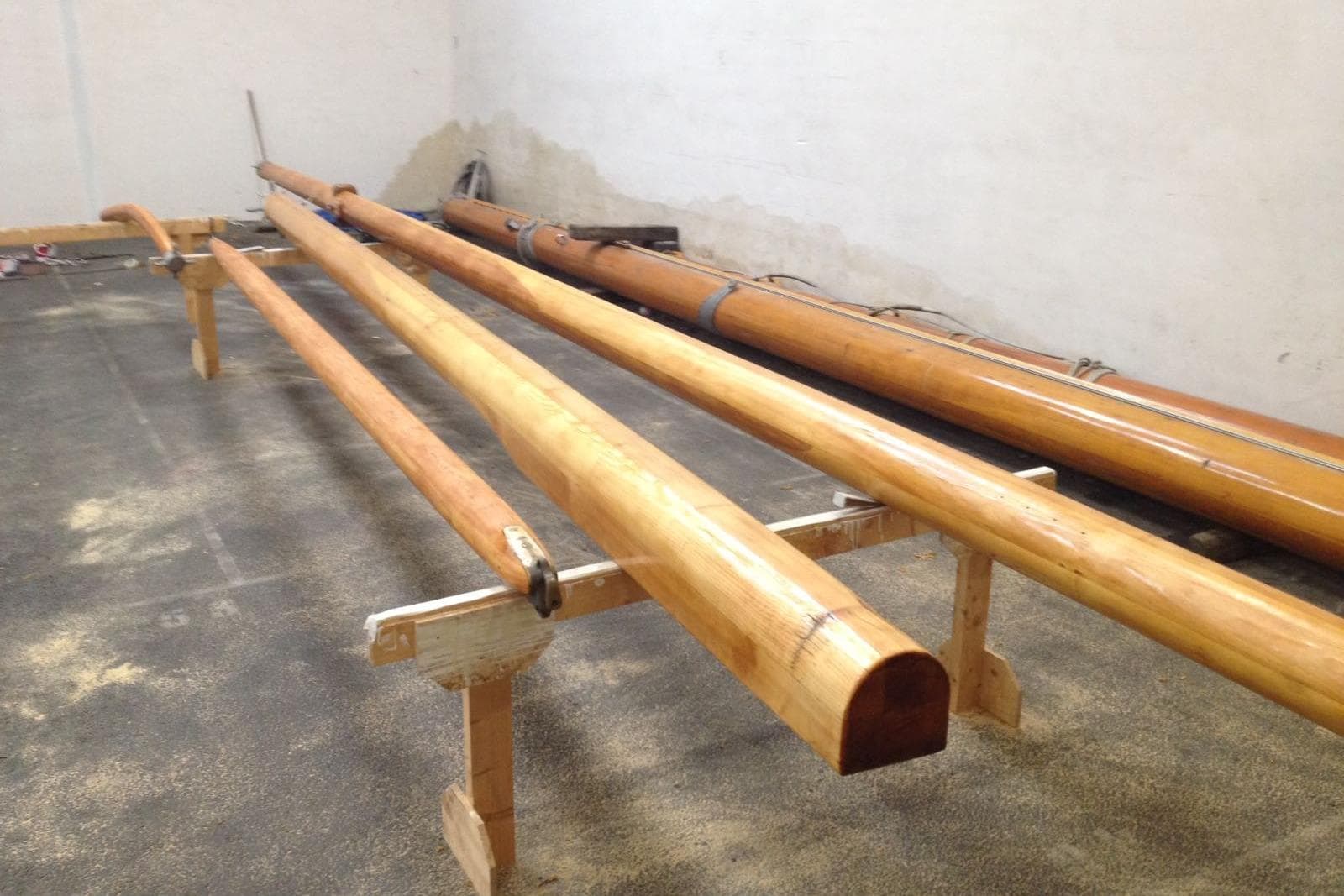 Wooden masts for 2025 Herreshoff Steel Hull boat, displayed indoors on supports.