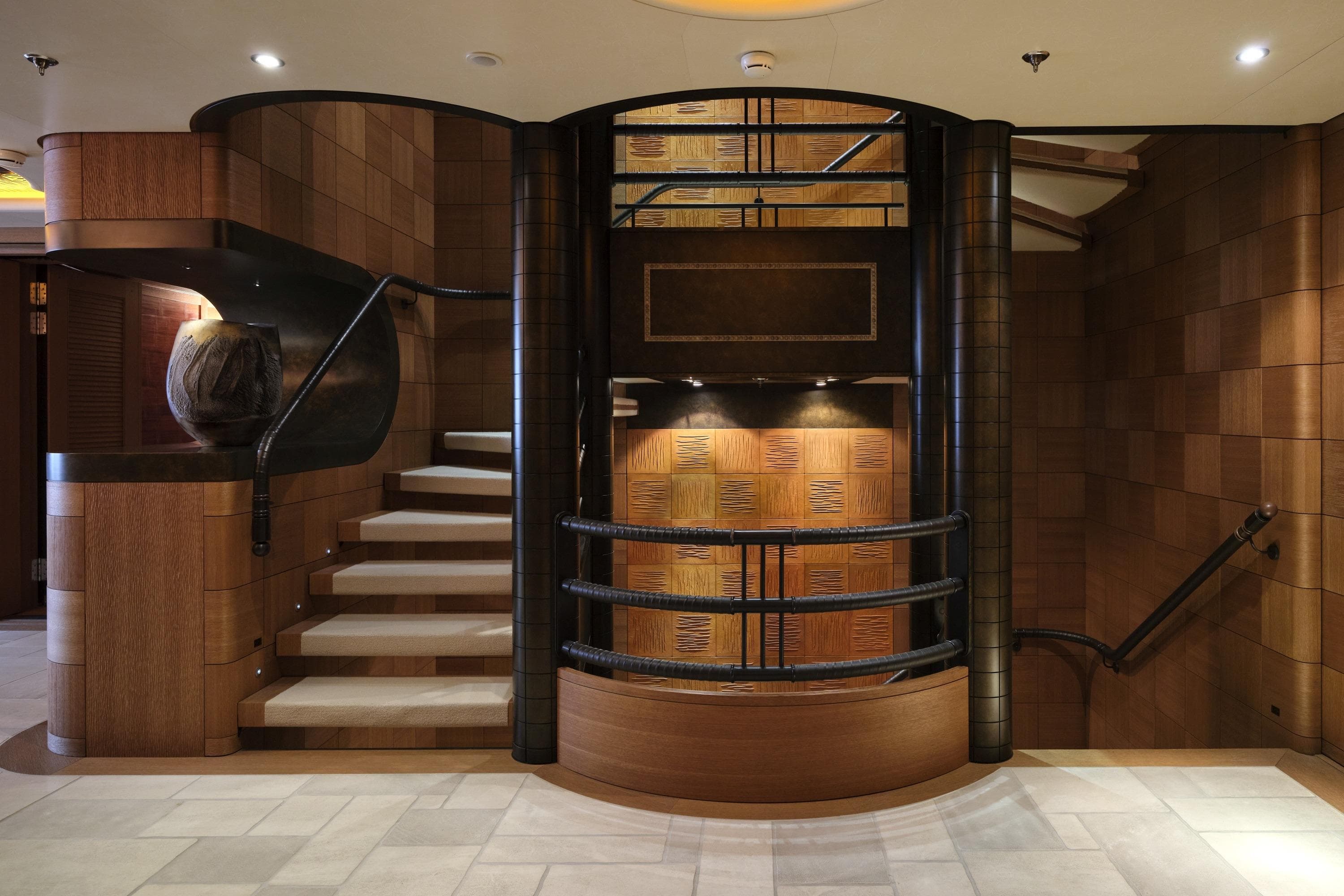 Luxurious interior staircase of a 2003 Lurssen fully custom-built yacht, featuring elegant wood paneling.
