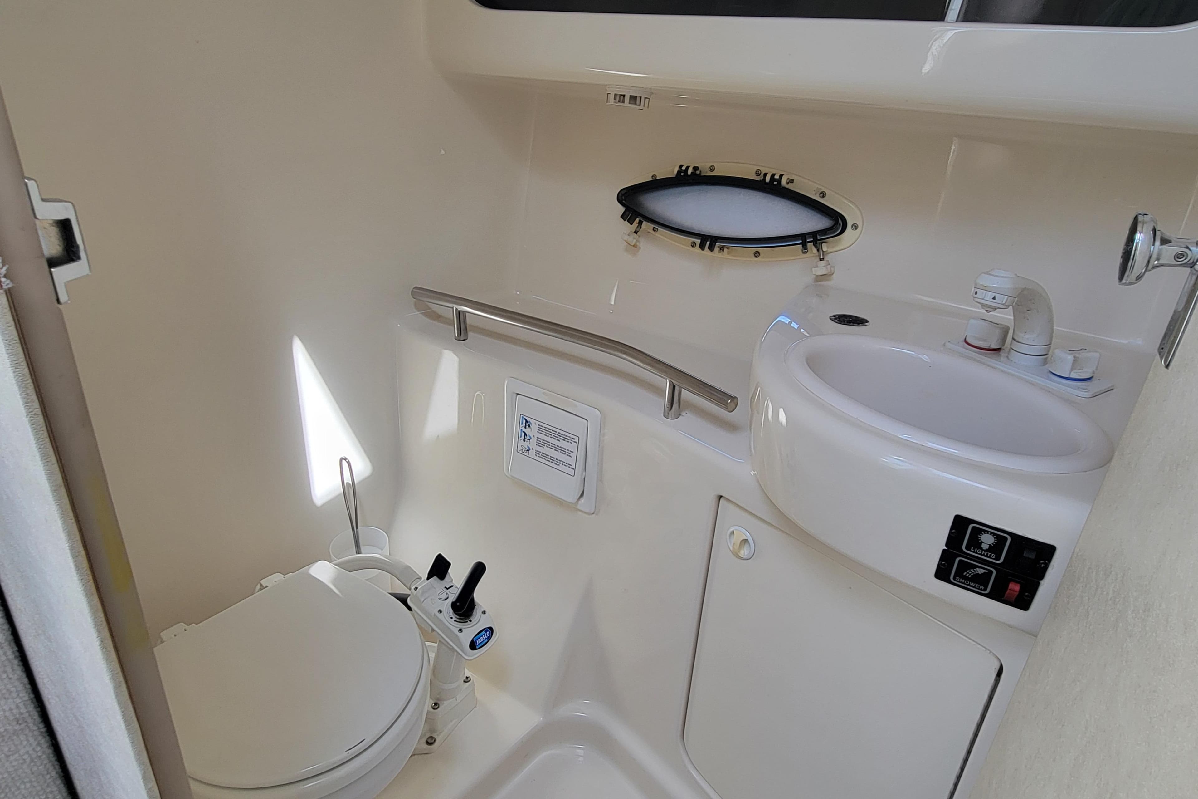 1999 Bayliner 3055 Ciera Sunbridge bathroom with toilet, sink, and porthole window.