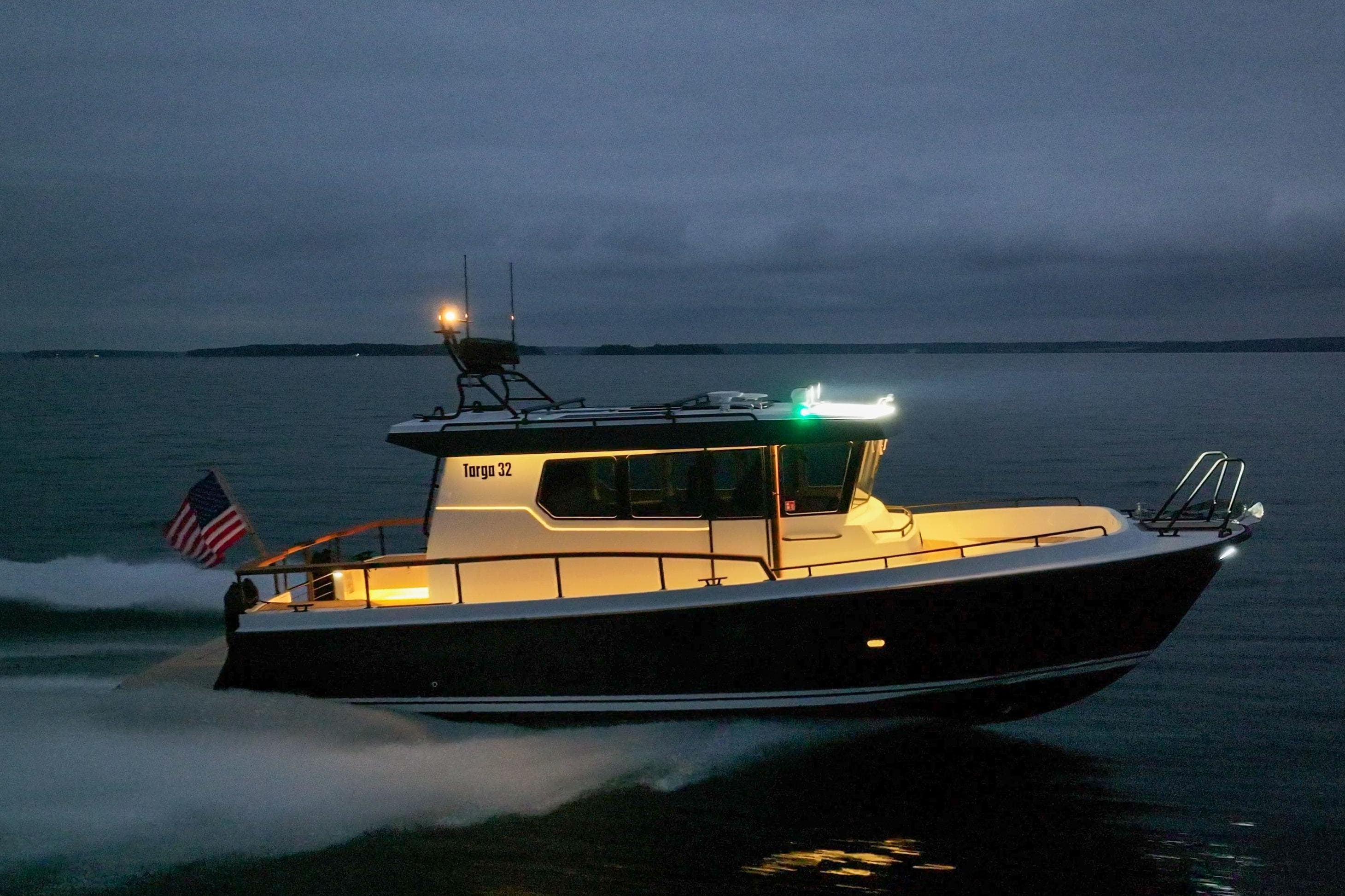 2027 Targa 32 boat cruising at dusk with illuminated cabin and American flag.
