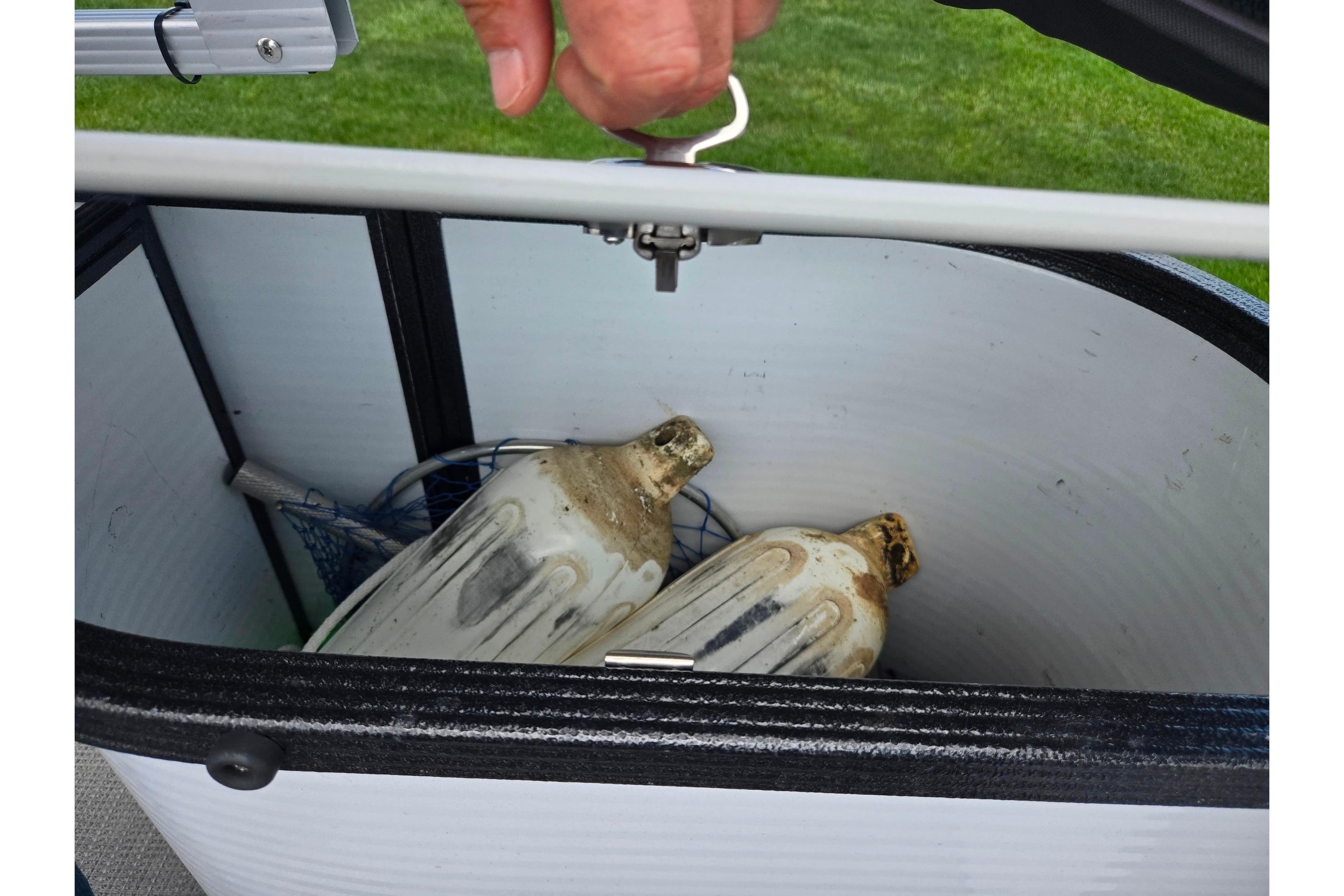 Open storage compartment on 2023 Crest Classic LX 200 boat with vintage jugs inside.