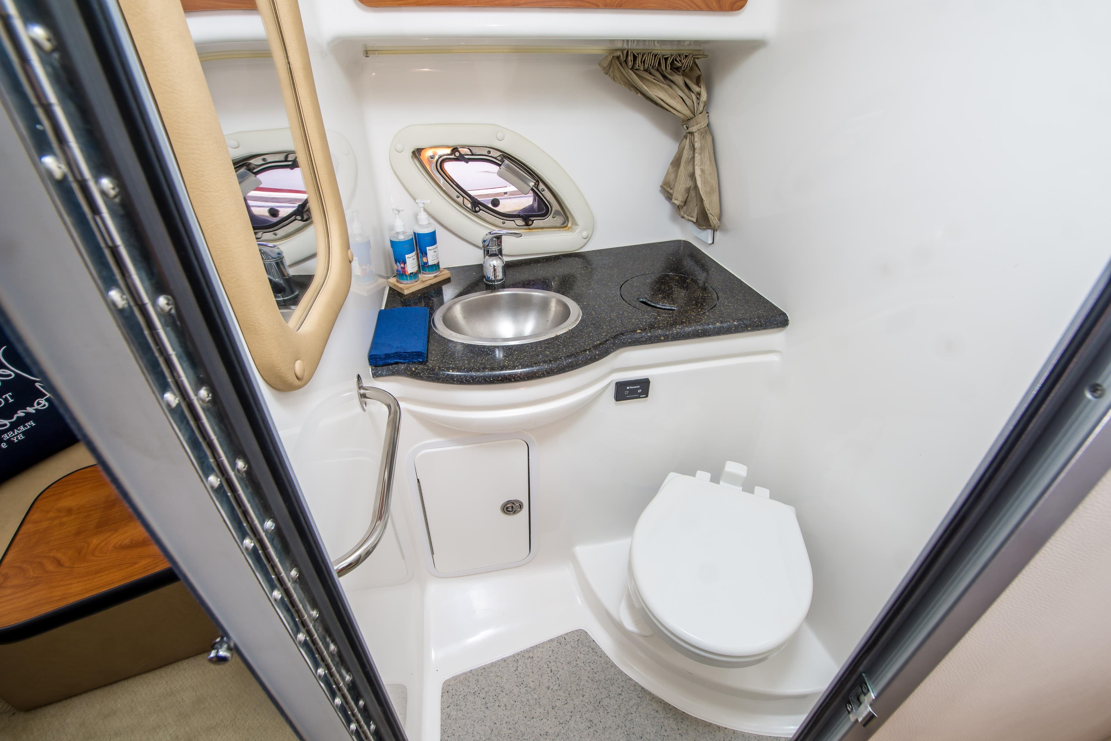 2012 Rinker 310 Express Cruiser bathroom with sink, toilet, and porthole window.