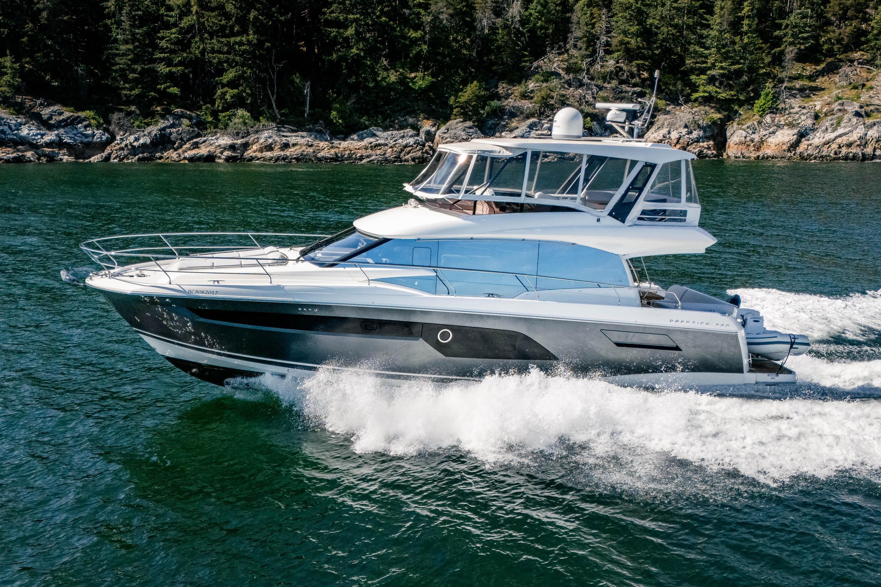 Luxury 2022 Prestige 520 yacht cruising on scenic waterway with forested shoreline.