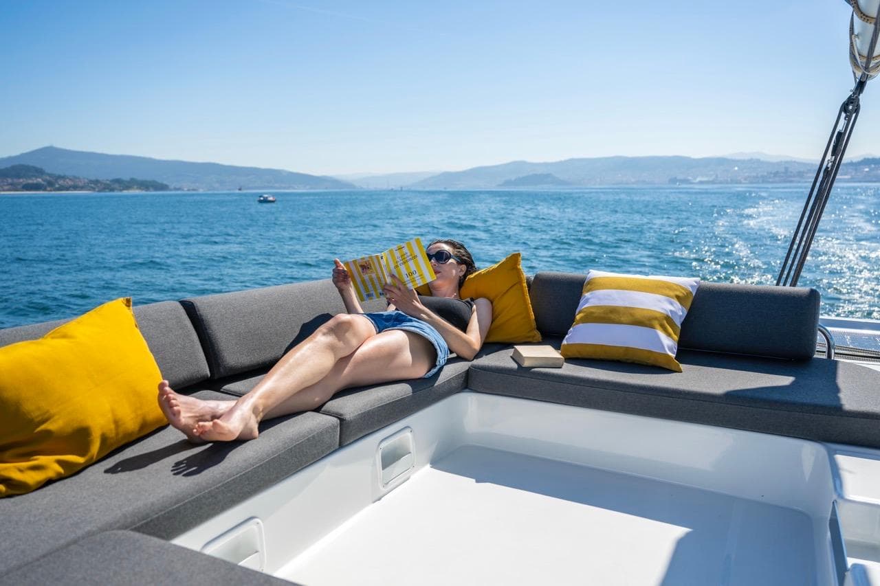 Woman relaxing on Lagoon 43 yacht, reading a book, with scenic ocean view.