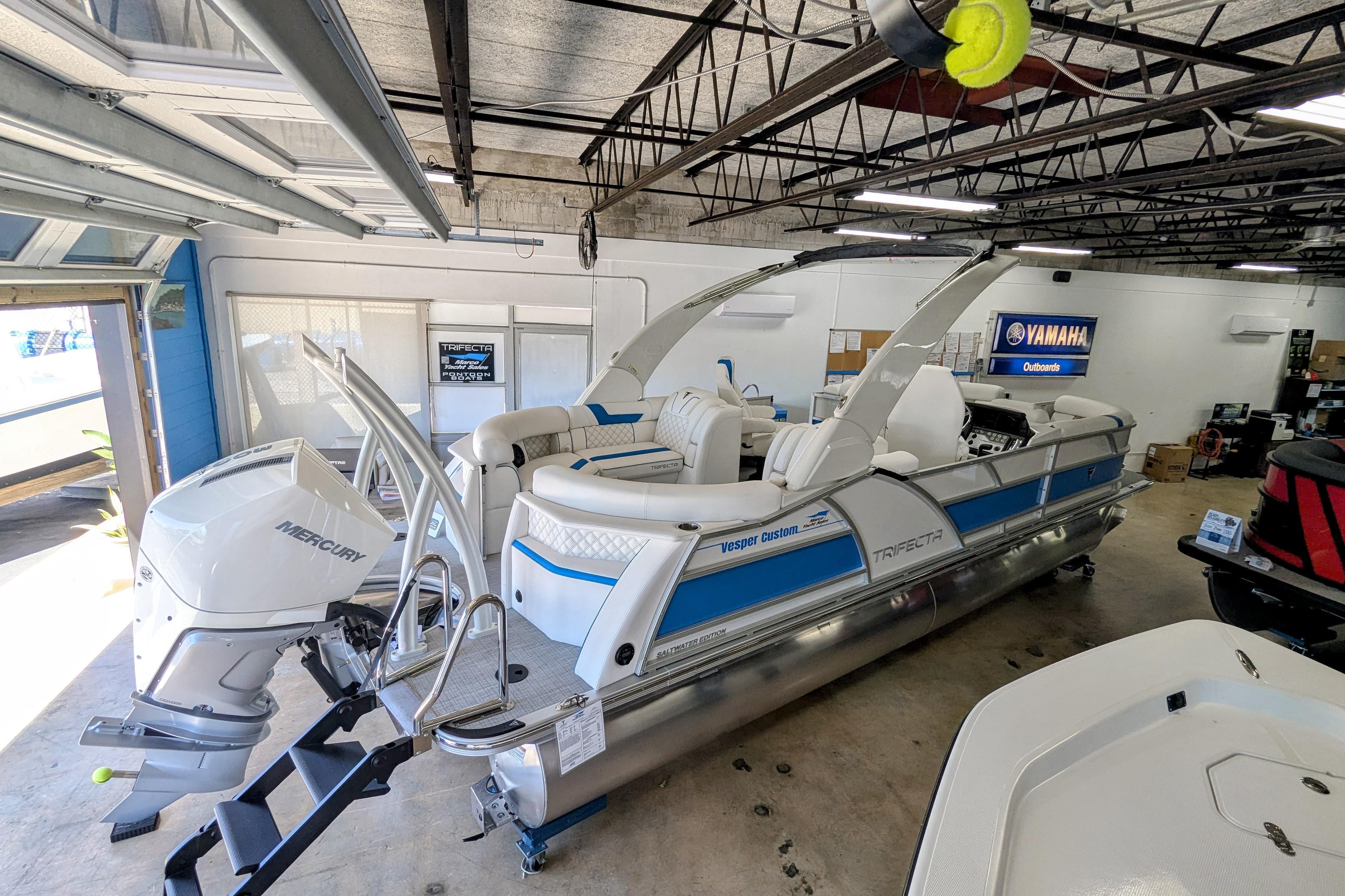 2026 Trifecta 25 RF SS Arch pontoon boat in showroom with Mercury outboard motor.