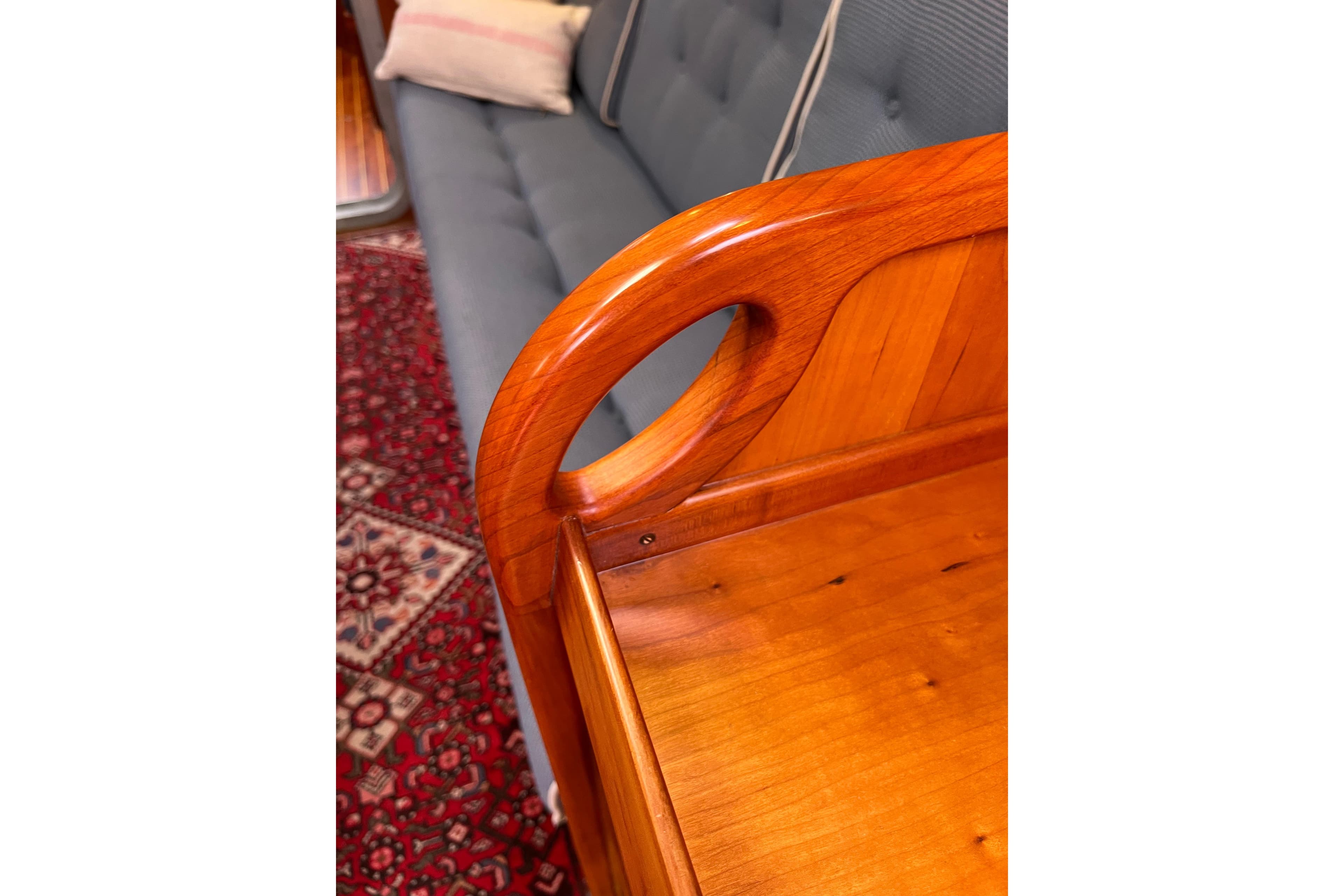 Polished wooden furniture detail with blue sofa and patterned red rug, Able Apogee 50, 1995.