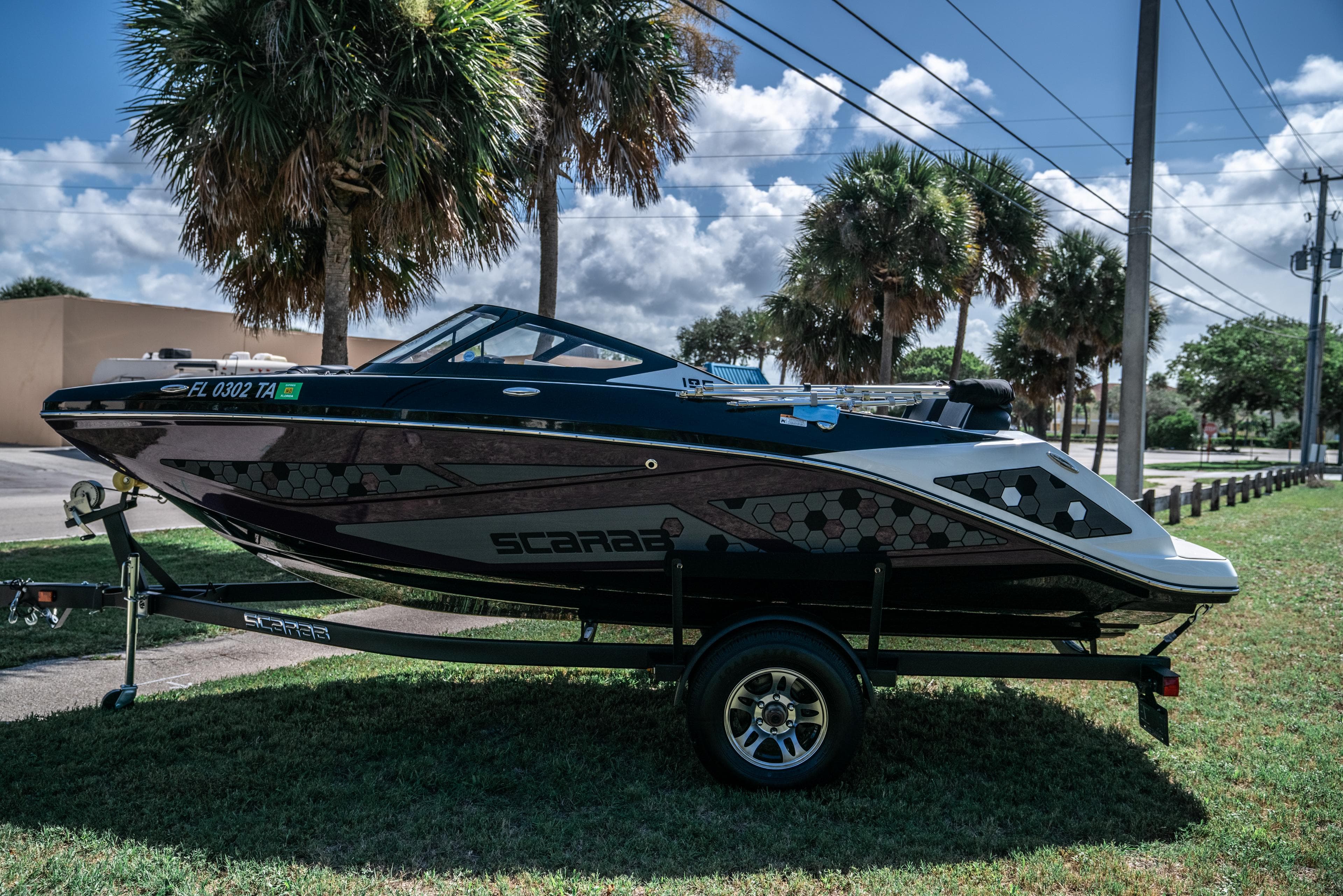 2021 Scarab 195 boat on a trailer, parked outdoors with palm trees in the background.