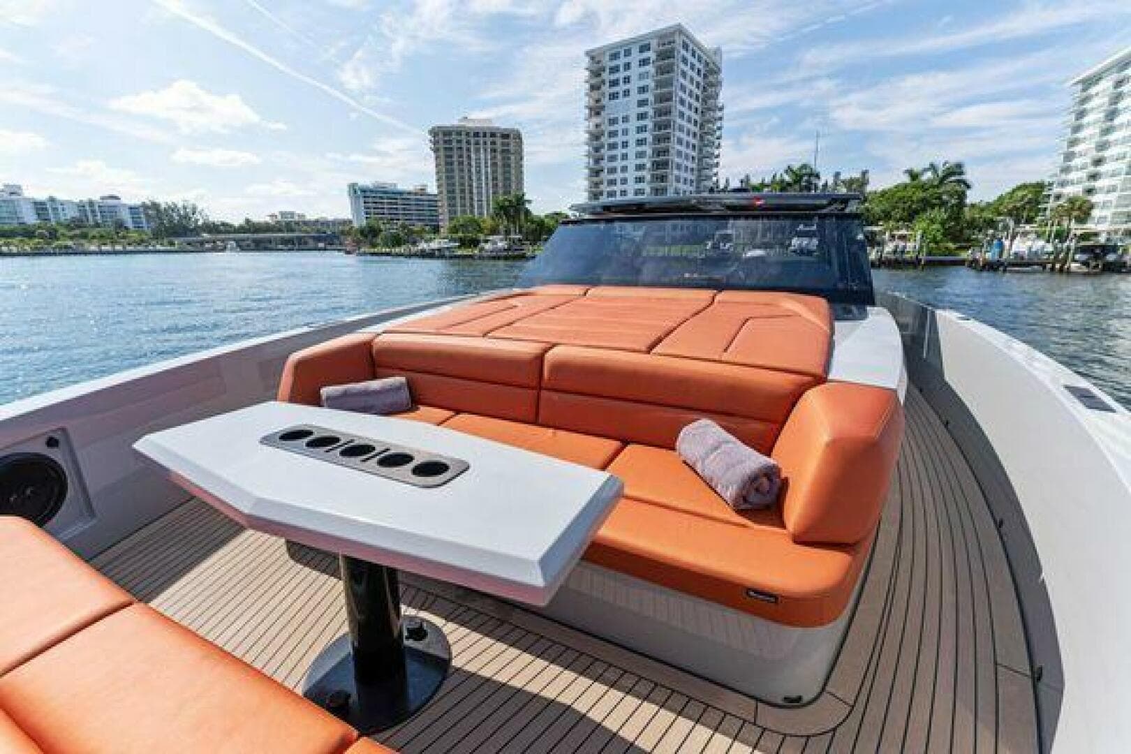 Luxurious 2021 Vanquish VQ58 yacht with orange seating, docked near waterfront buildings.