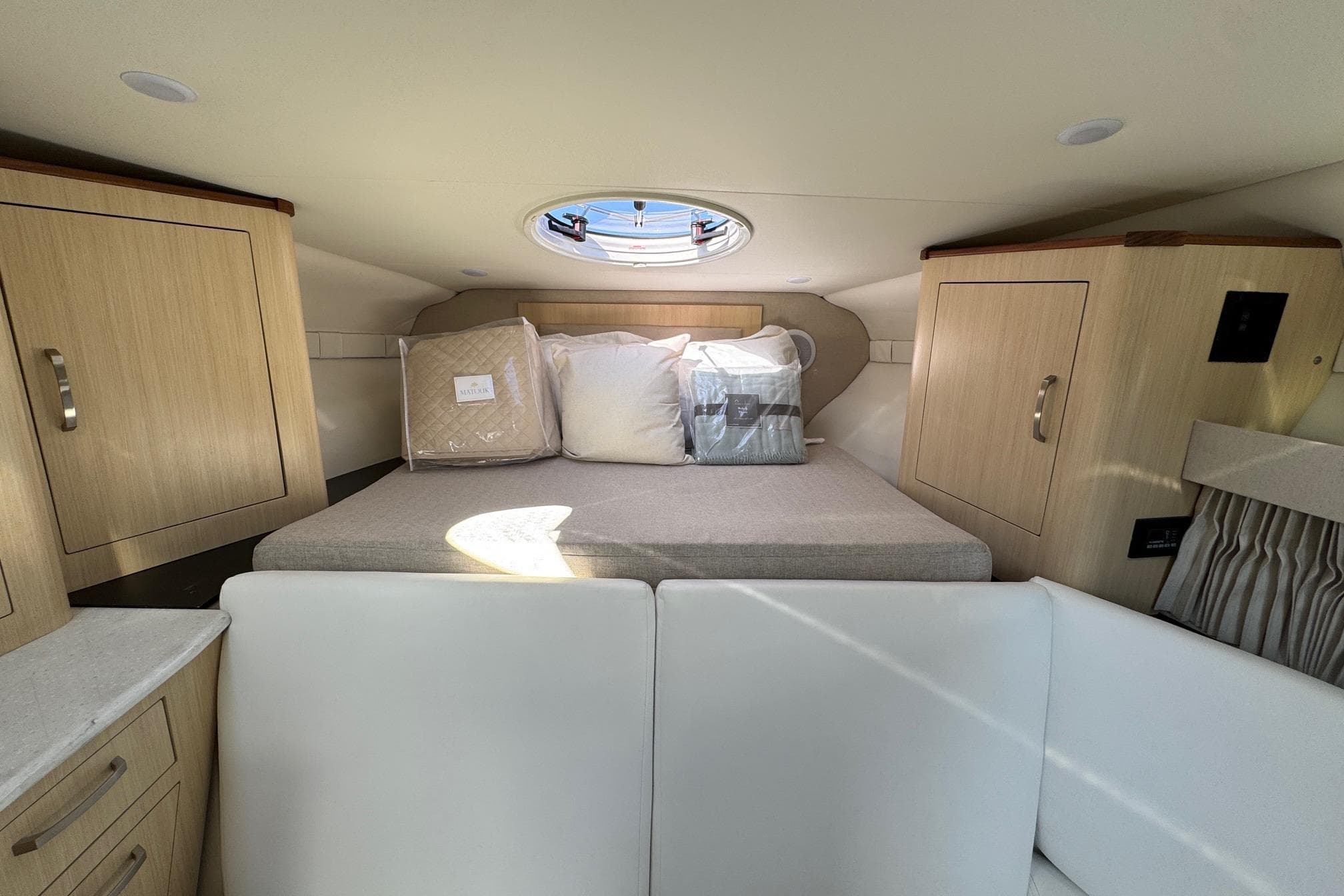 2026 Regal 33 XO cabin interior with bed, wooden cabinets, and porthole window.