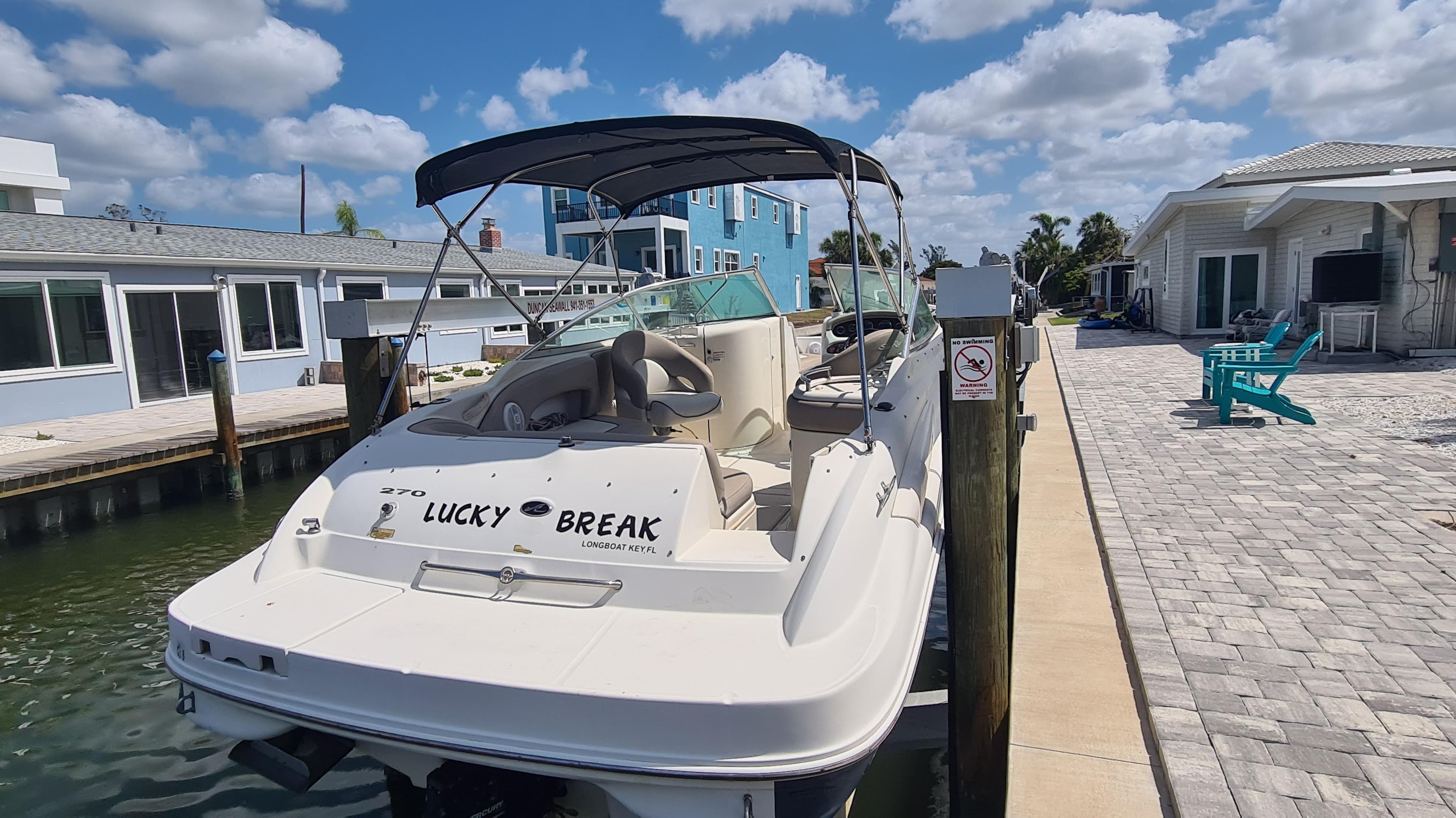 2004 Sea Ray 270 Sundeck boat docked by waterfront homes under a blue sky.