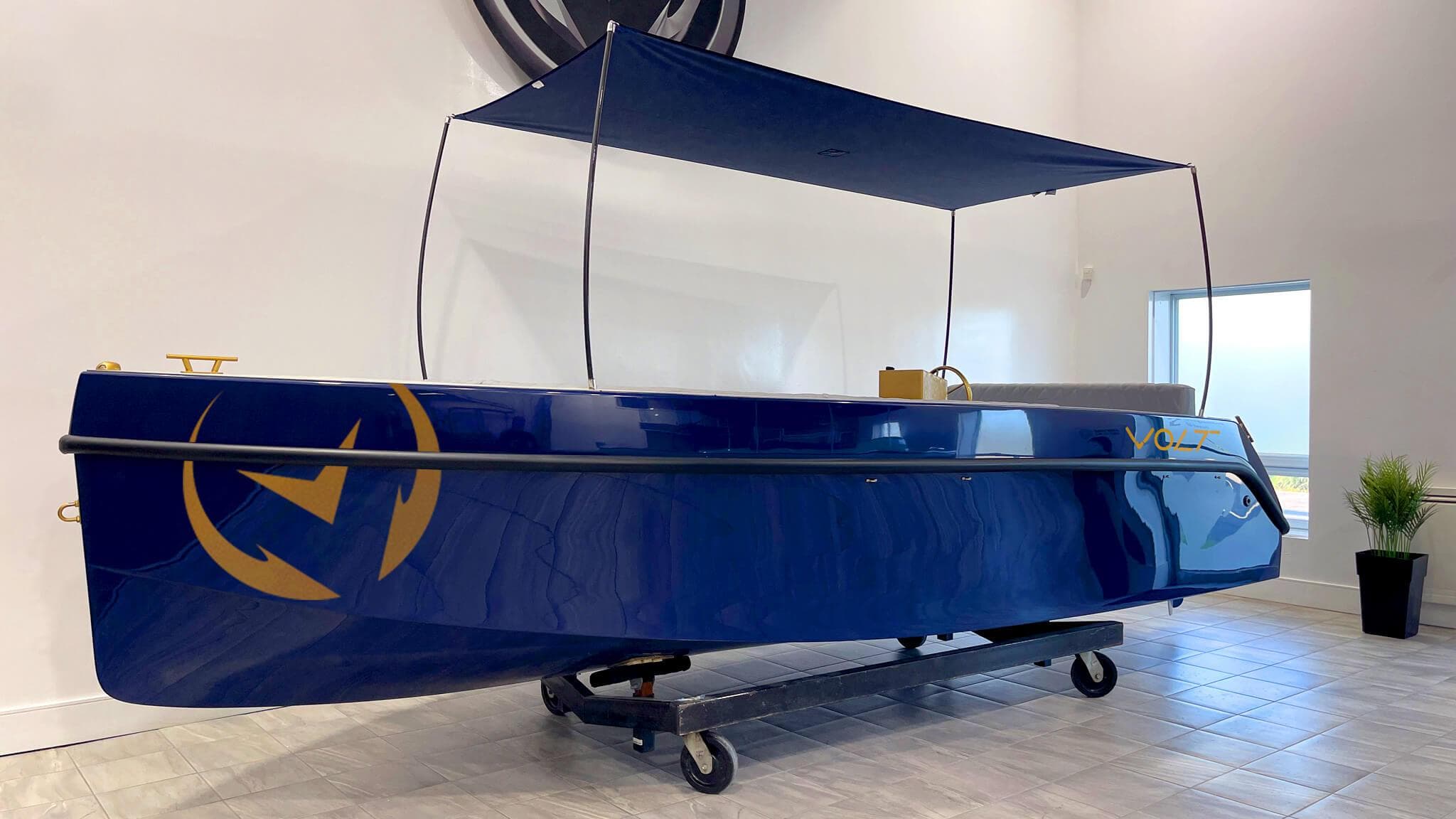 2023 Vision Marine Technologies Volt 180 electric boat, blue with canopy, displayed indoors.