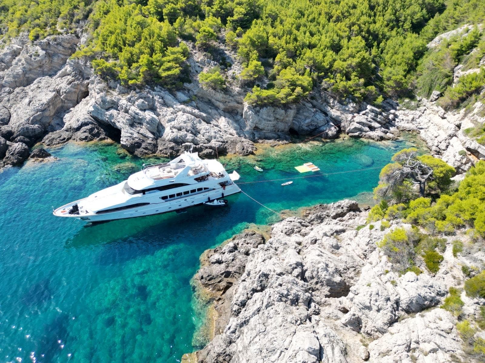 Luxurious Benetti Classic 115 yacht anchored in a serene, rocky cove with clear turquoise waters.